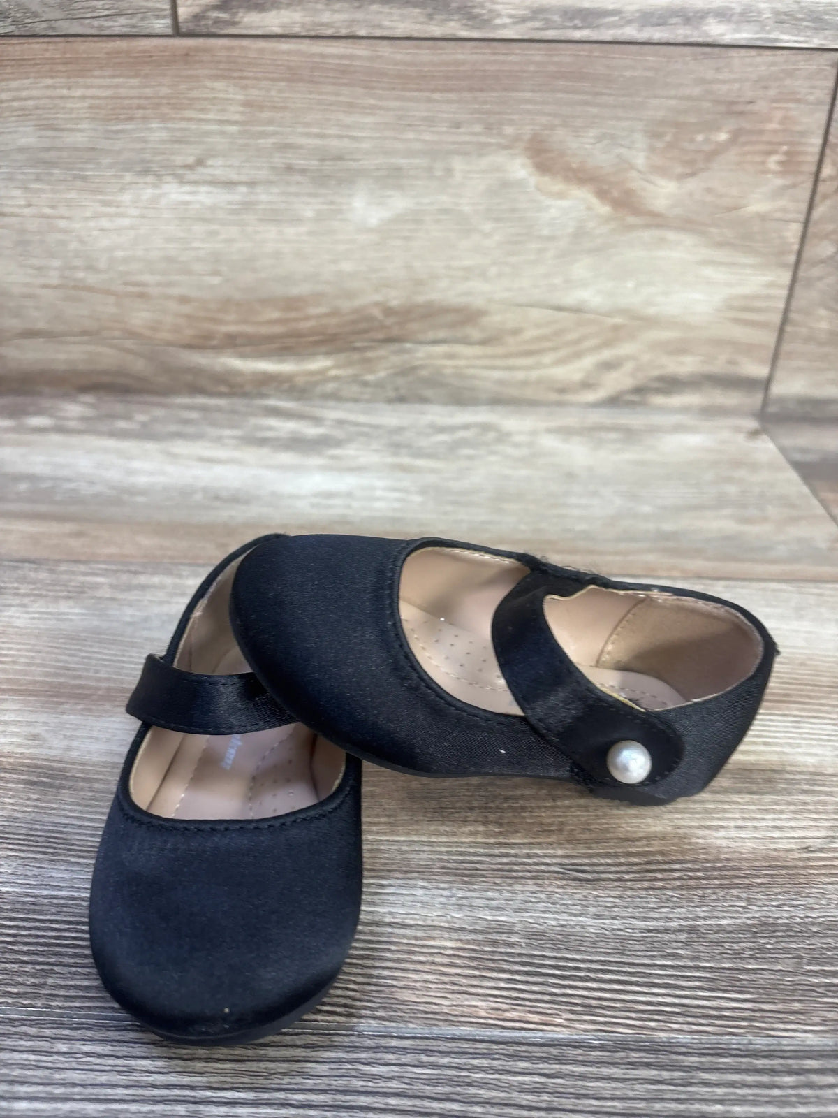 Angled view of black FunkyMonkey Mary Jane ballet flats showcasing rounded toes and Velcro straps on a wood-look floor