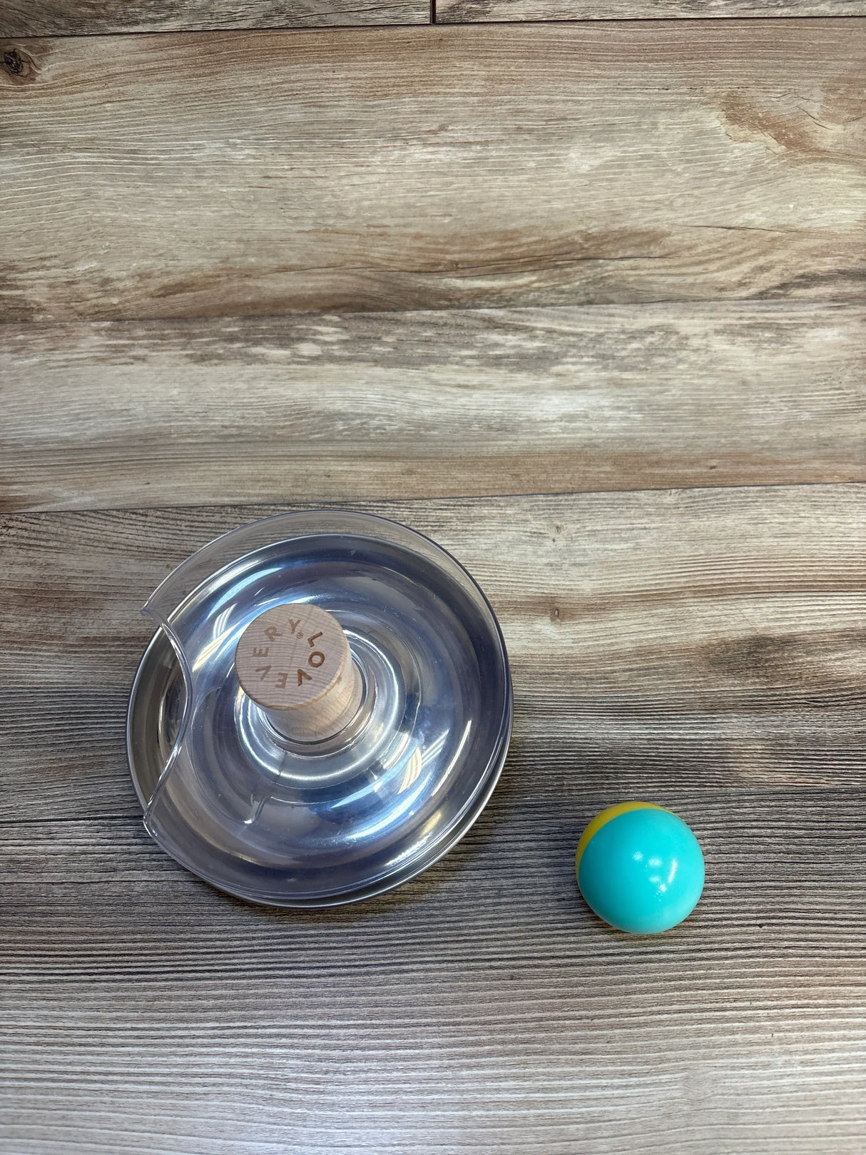 Clear baby activity toy with wooden base and colorful ball on wood floor