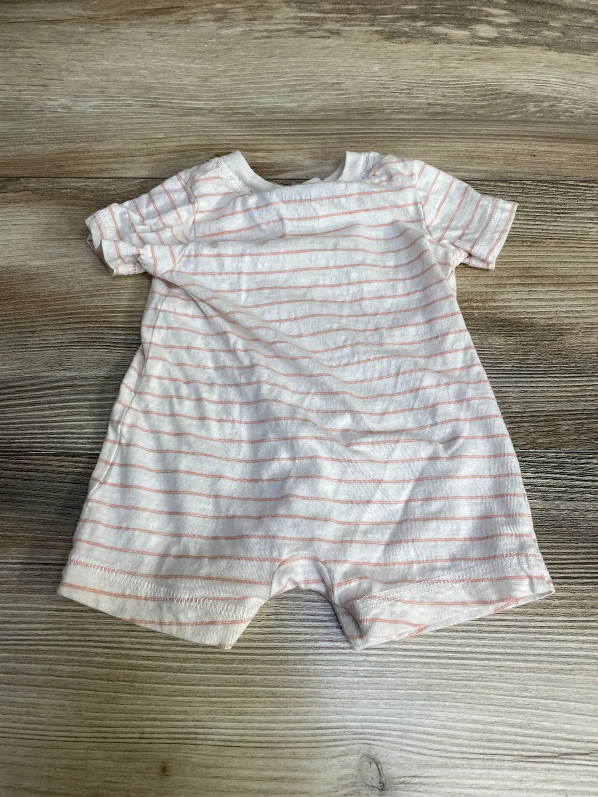 Flat lay of Carter’s newborn striped Henley romper showing short sleeves and thin pink stripes on a wood background
