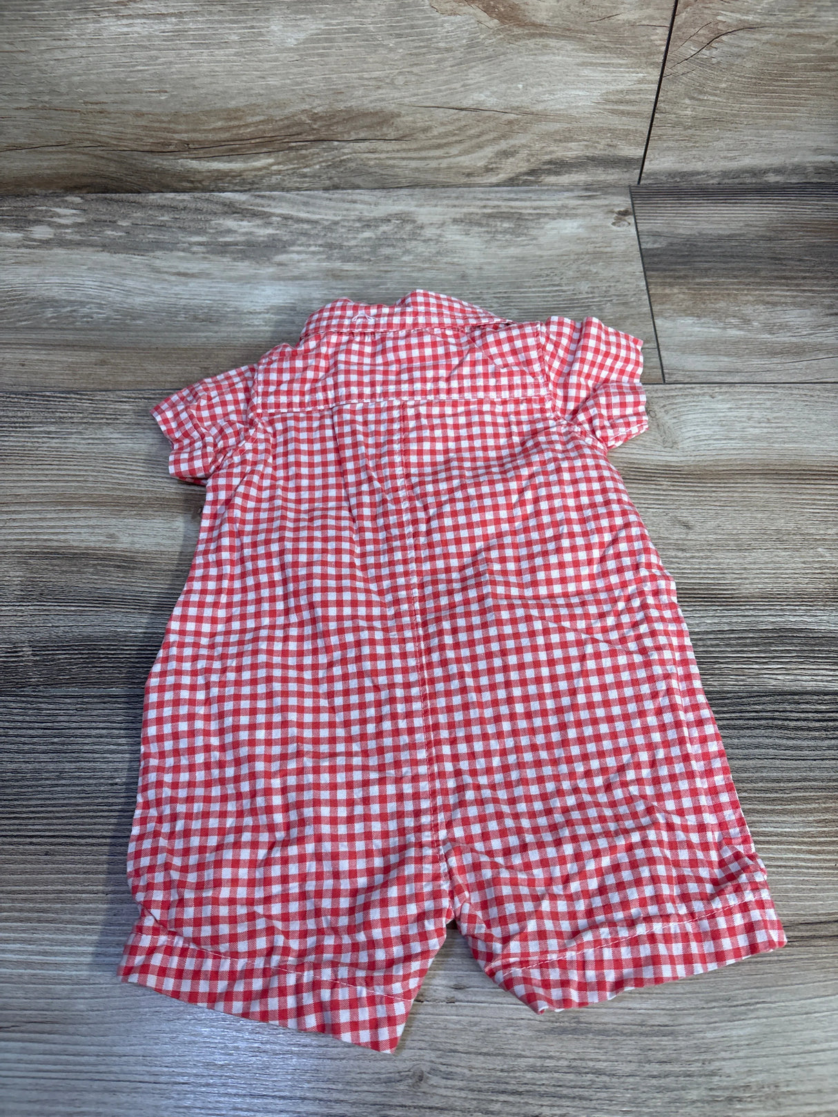 Back view of red and white gingham shortie romper showing short sleeves, collar and cuffed short legs on wood floor background