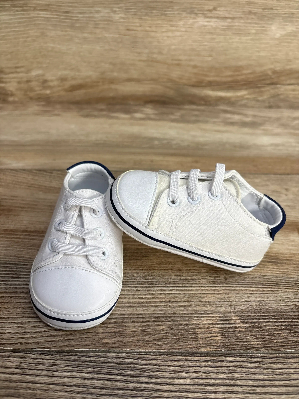Side view of Janie and Jack Boat Shoes in white with navy trim and lace-up front on wood plank floor