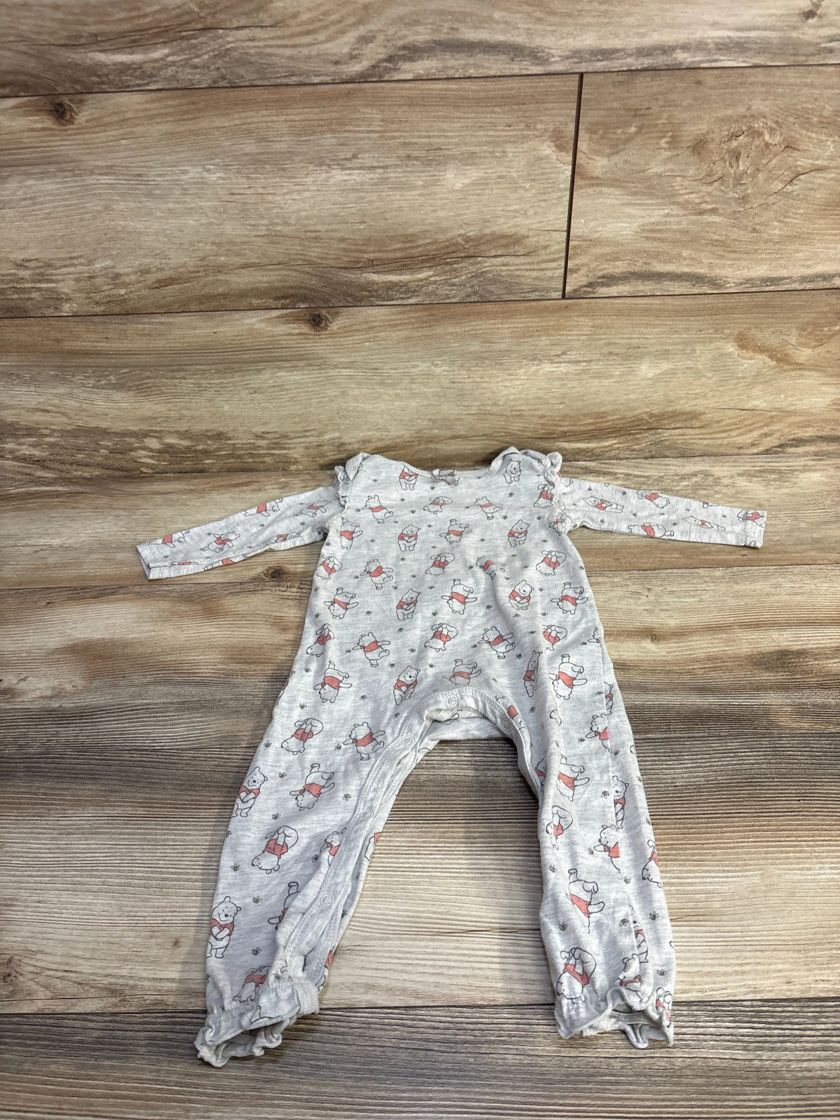 Front flat lay of grey Disney Winnie the Pooh coverall 18 months showing all-over Pooh print, long sleeves, snap leg closures and ruffle ankle cuffs on wood background