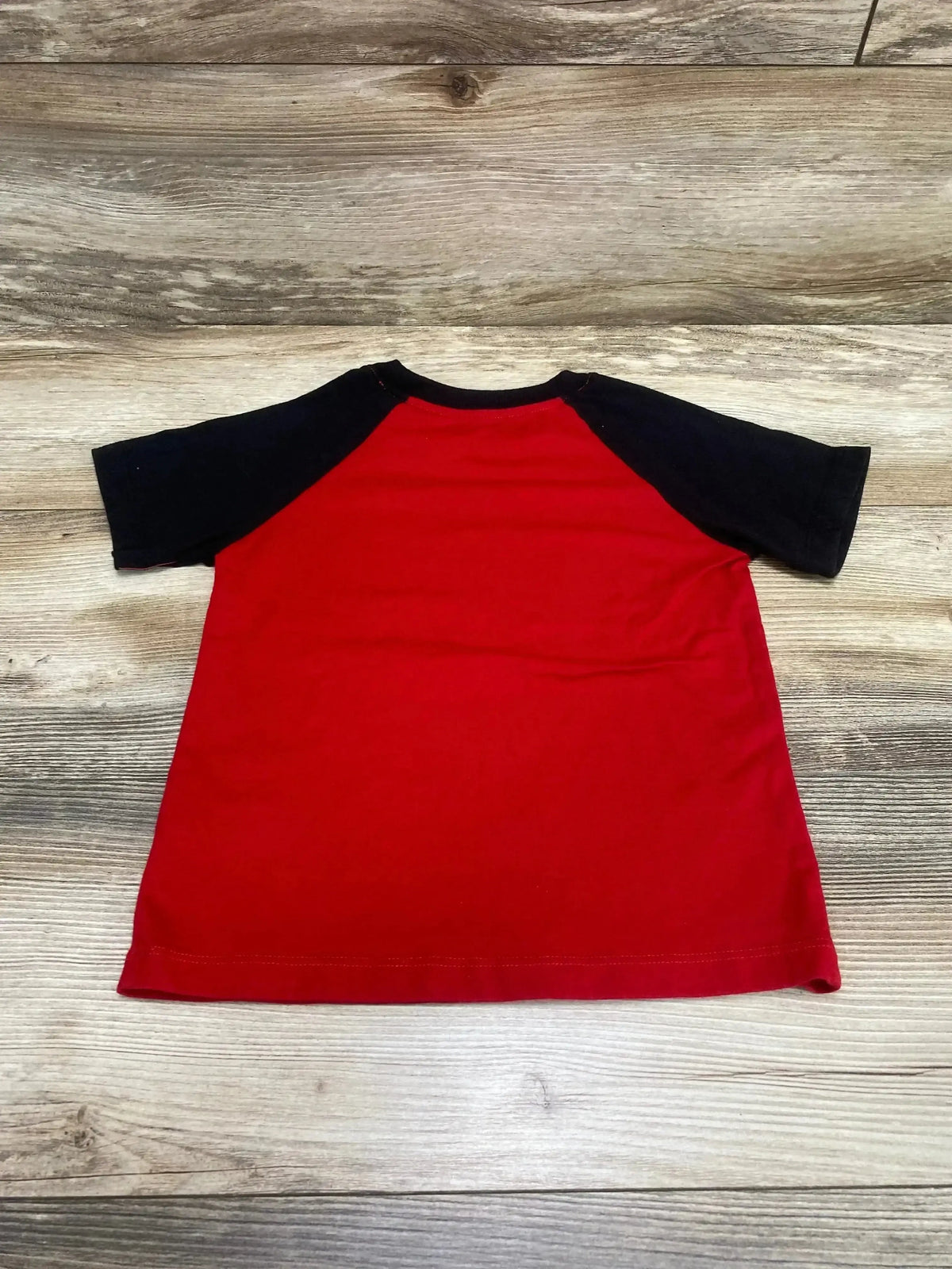 Back view of Celebrate Love Bug raglan shirt showing red body and black sleeves, laid flat on wood background, size 5T