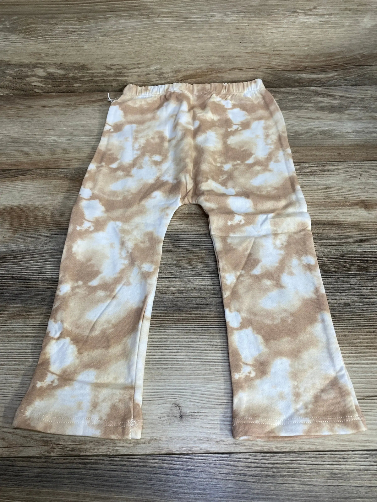 Flat lay of toddler tie-dye pants (brown and white), size 3T, showing elastic waistband and slight flare on wood background