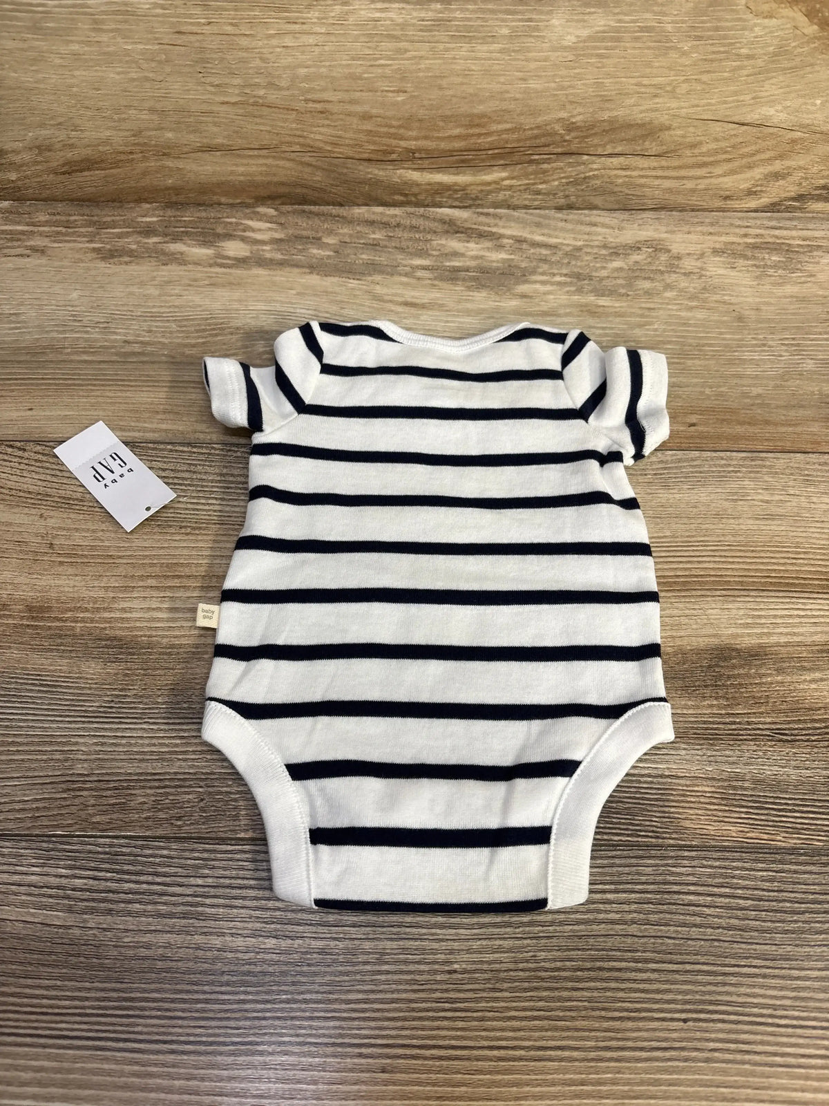Front view of newborn Baby Gap 100% cotton striped bodysuit showcasing navy stripes and short sleeves on a wood background