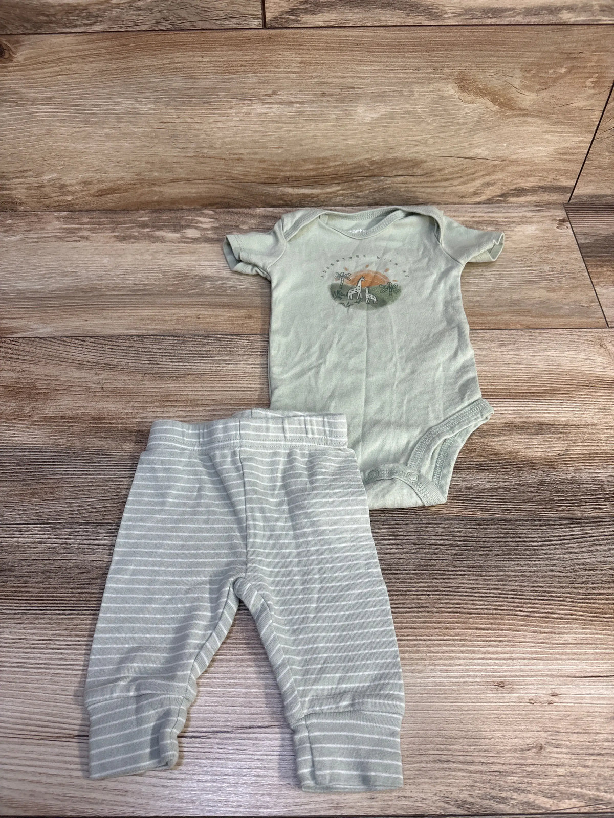 Top-down view of green Just One You bodysuit and matching striped pants set showcasing an animal graphic on wood background