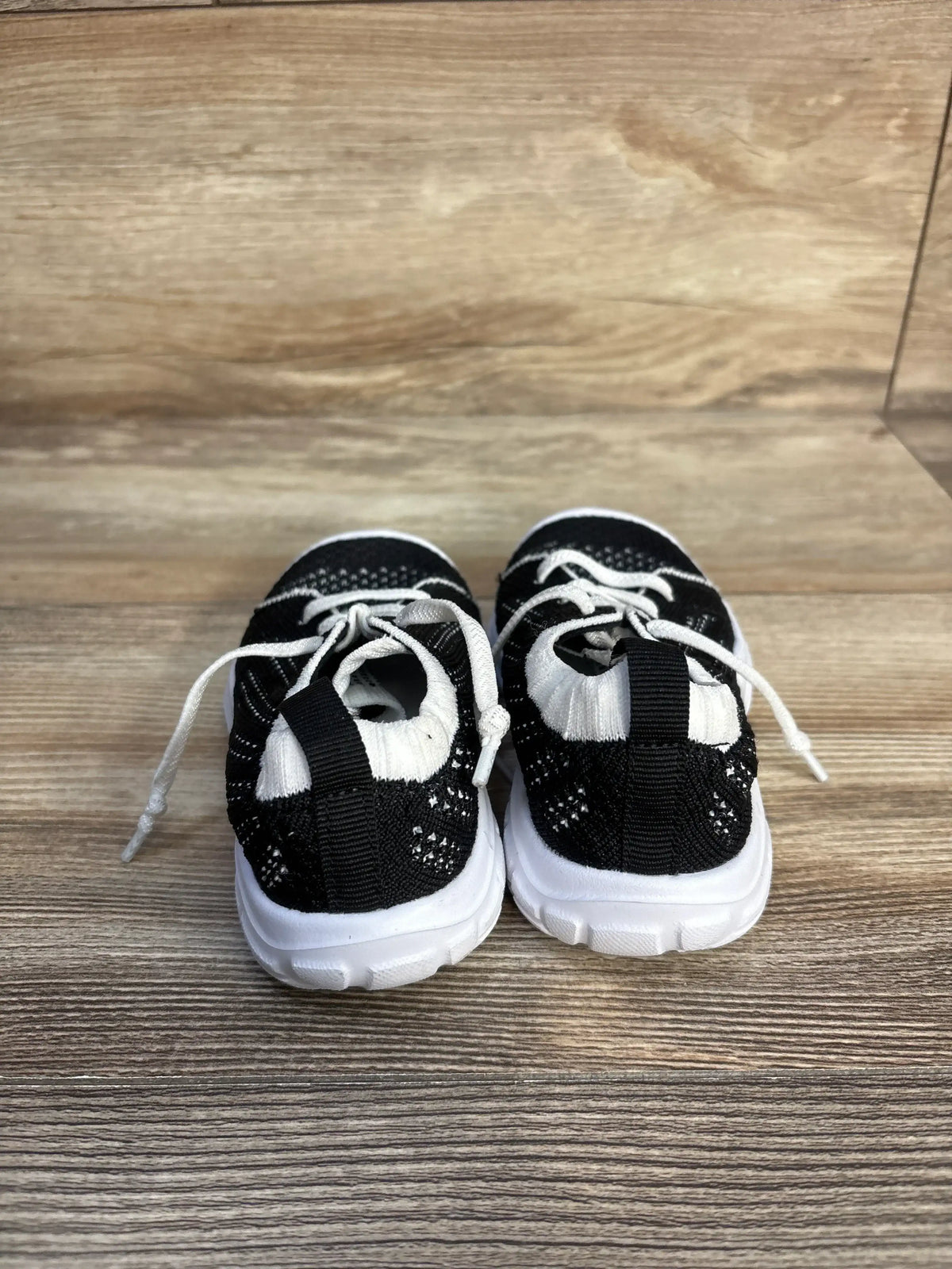 Rear view of Eqw slip-on sneakers in black showcasing knit uppers and white soles on a wood floor