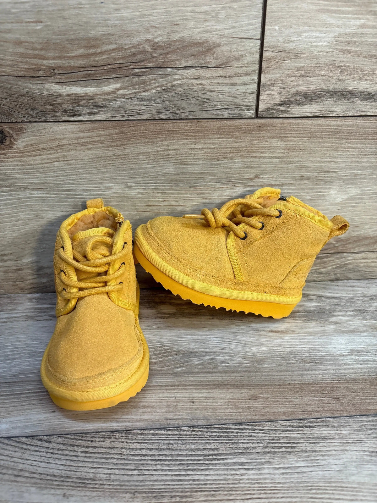 Three-quarter view of NWOT Ugg Neumel II Boots yellow sz 8c showcasing mustard suede upper laces and matching rubber sole on wood plank background