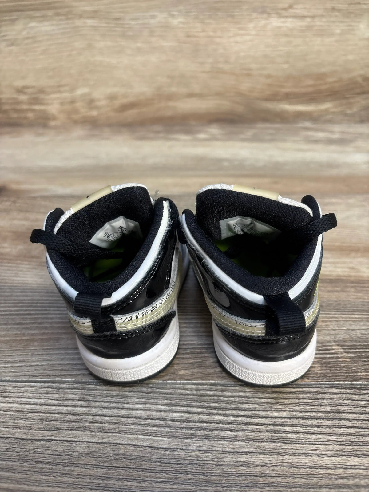 Back view of Air Jordan 1 Mid SE TD DIY Sneakers sz 4c showcasing black and white leather heel panels neon yellow lining and black laces on wood plank background
