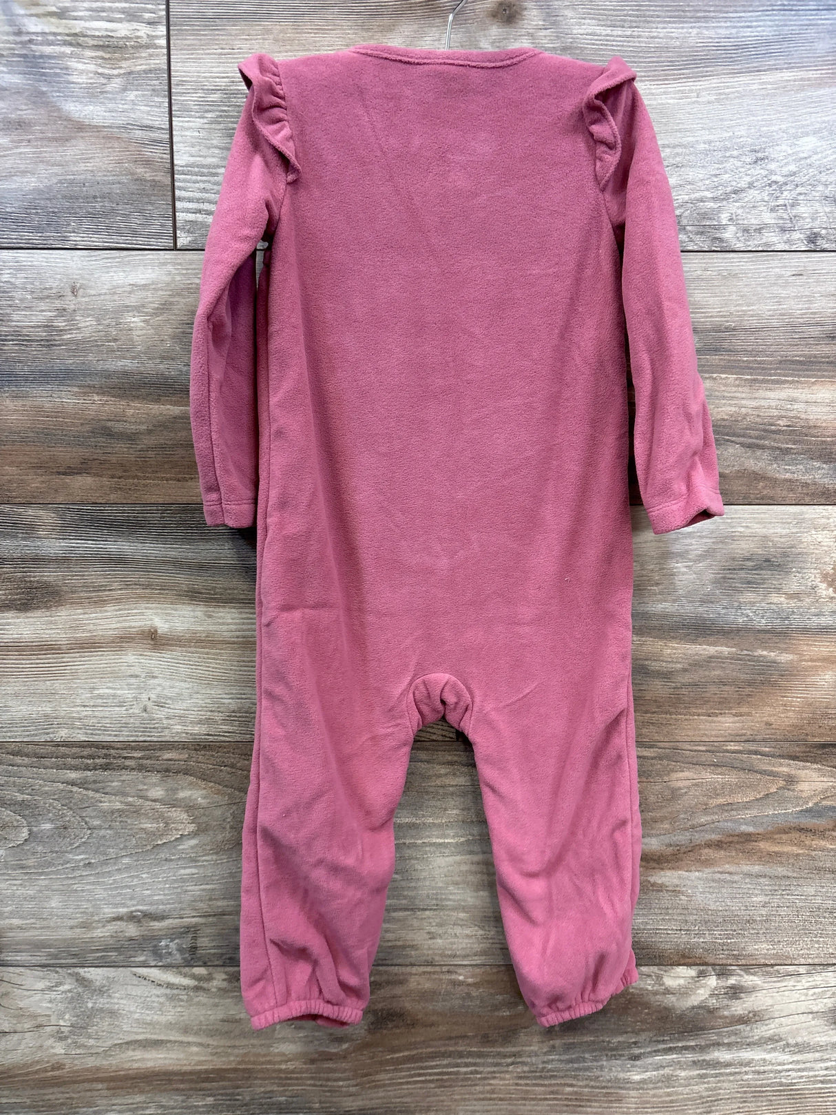Back view of pink long-sleeve fleece baby onesie with ruffle details on wooden floor