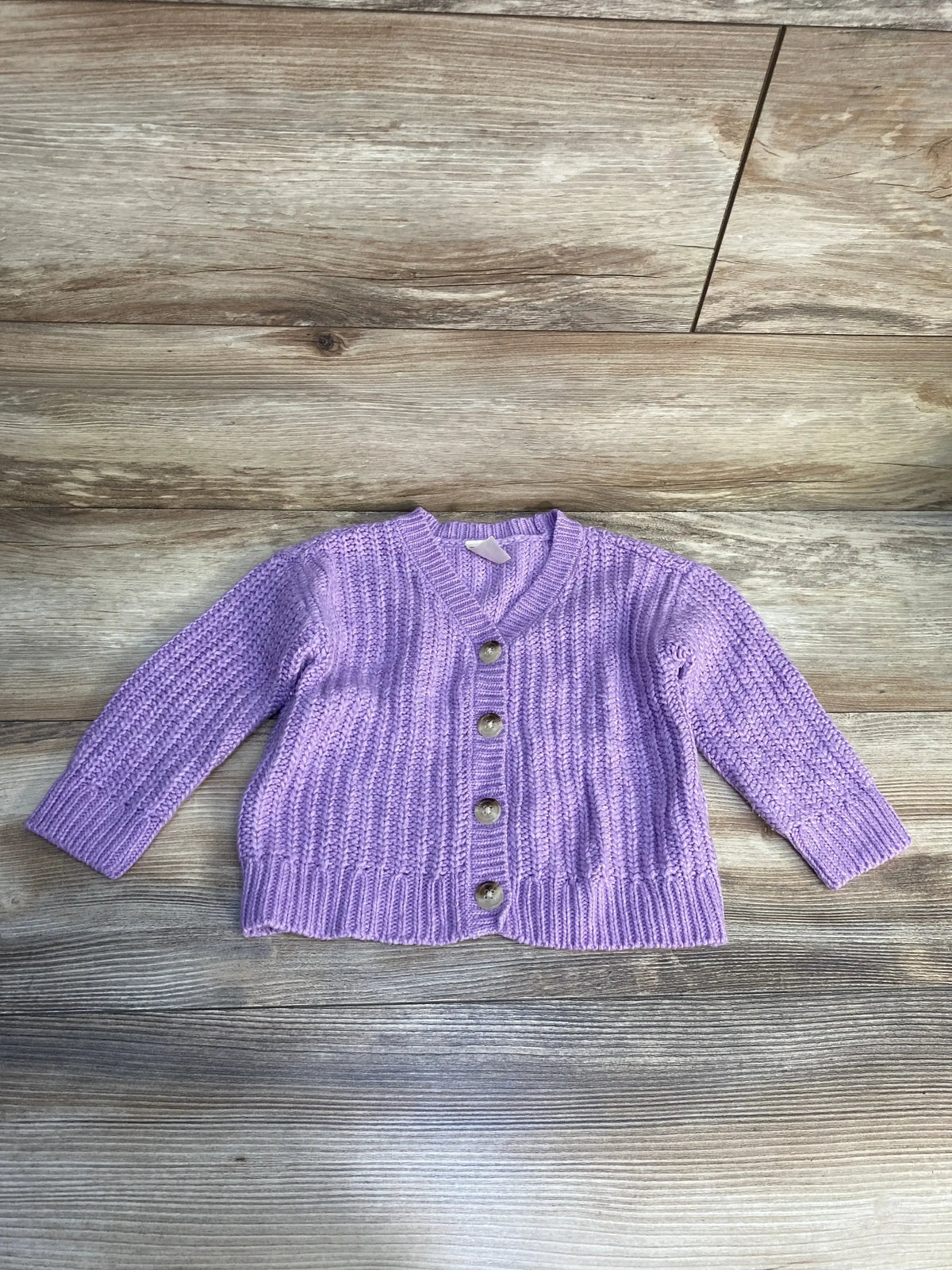 Purple knit baby cardigan with buttons on wood background