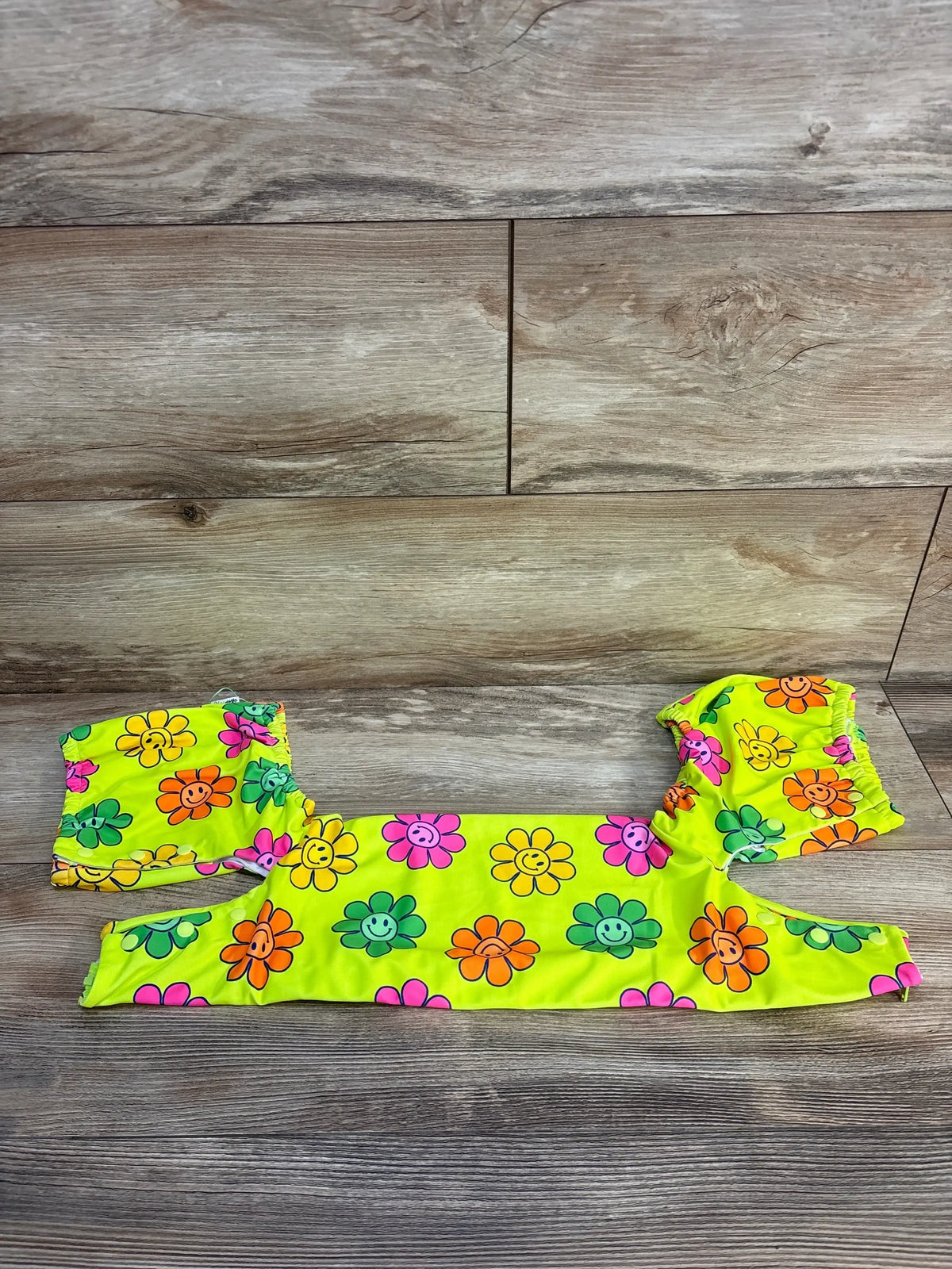 Flat lay of Gigi and Max Flower floatie cover showing bright yellow fabric with multicolored smiley-face flowers on wooden background