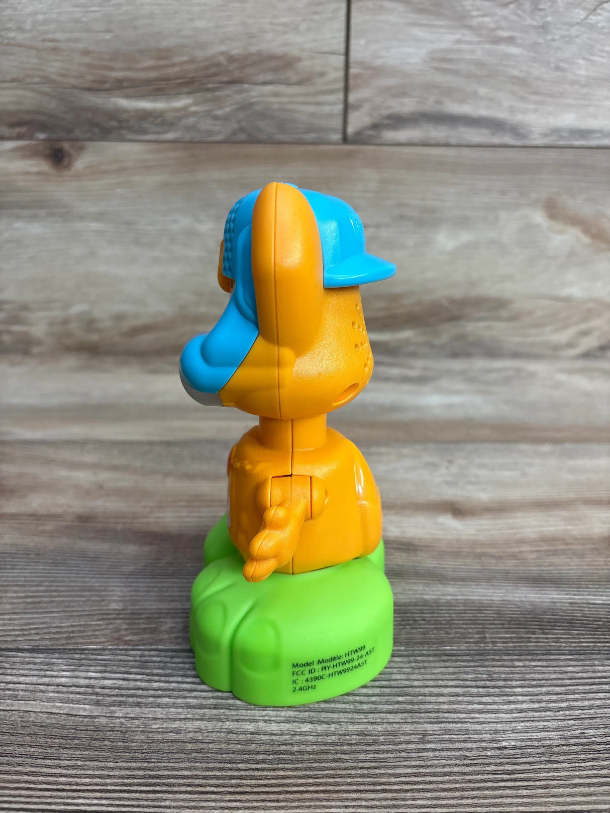 Side view of Fisher-Price Link Squad Opposites Fox Toy in orange with blue cap on green base on wood plank floor