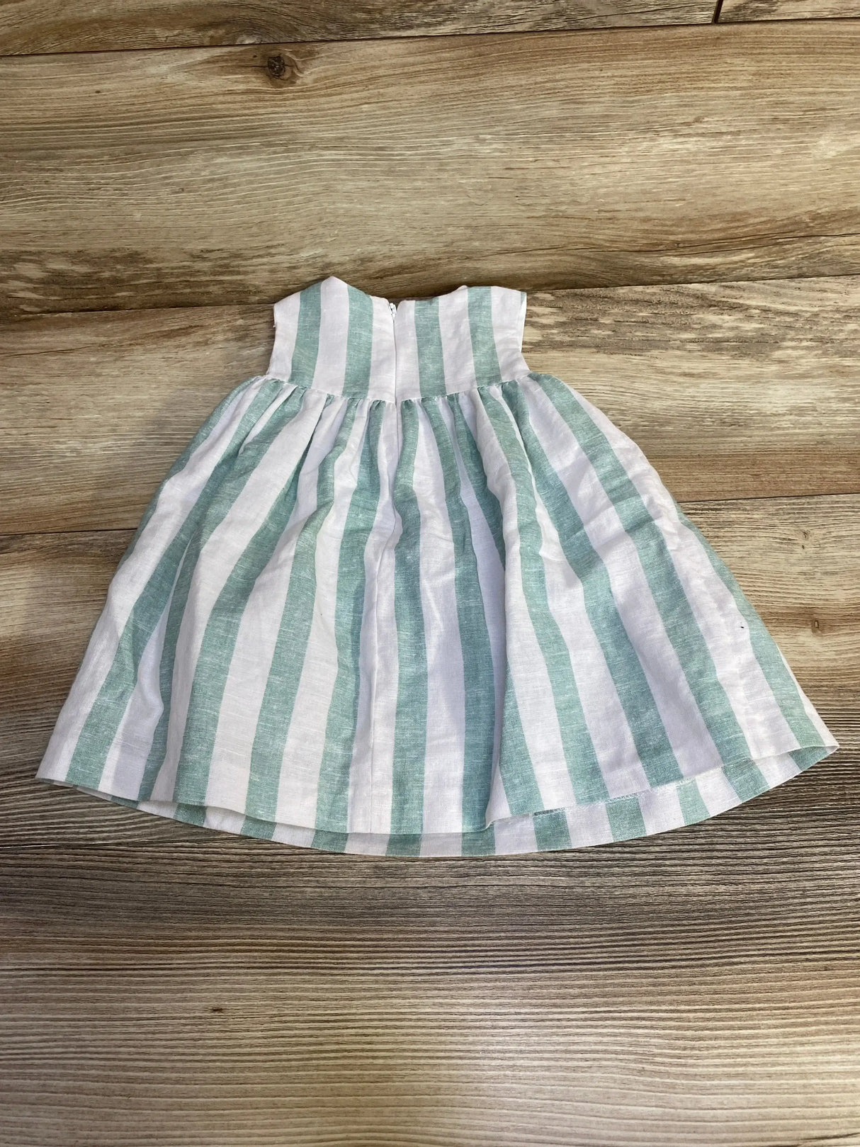 Flat lay of baby striped linen dress with mint and white vertical stripes, gathered skirt and back zipper on wood background