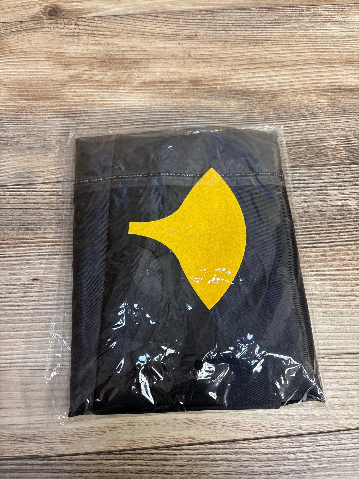 Black kids t-shirt with yellow graphic, sealed in plastic on wood surface