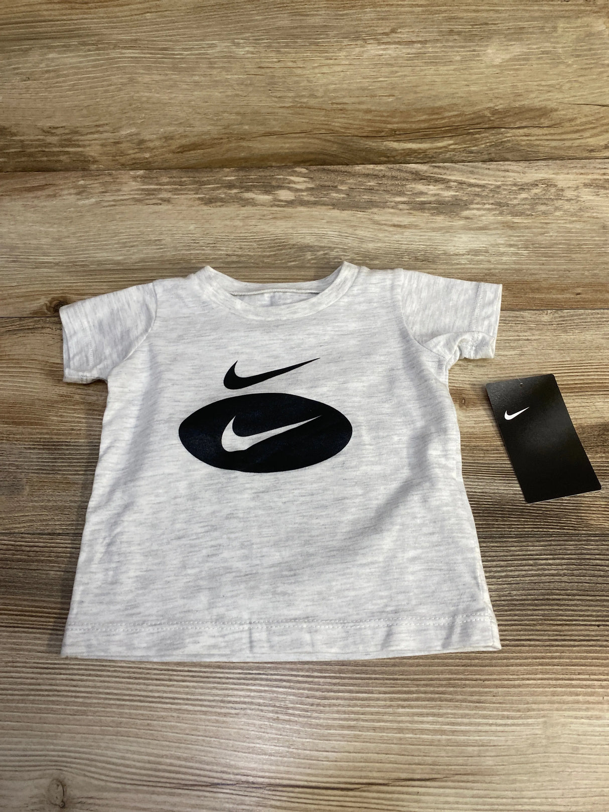 Light gray toddler Nike t-shirt with black swoosh logos and a black Nike tag on wooden surface