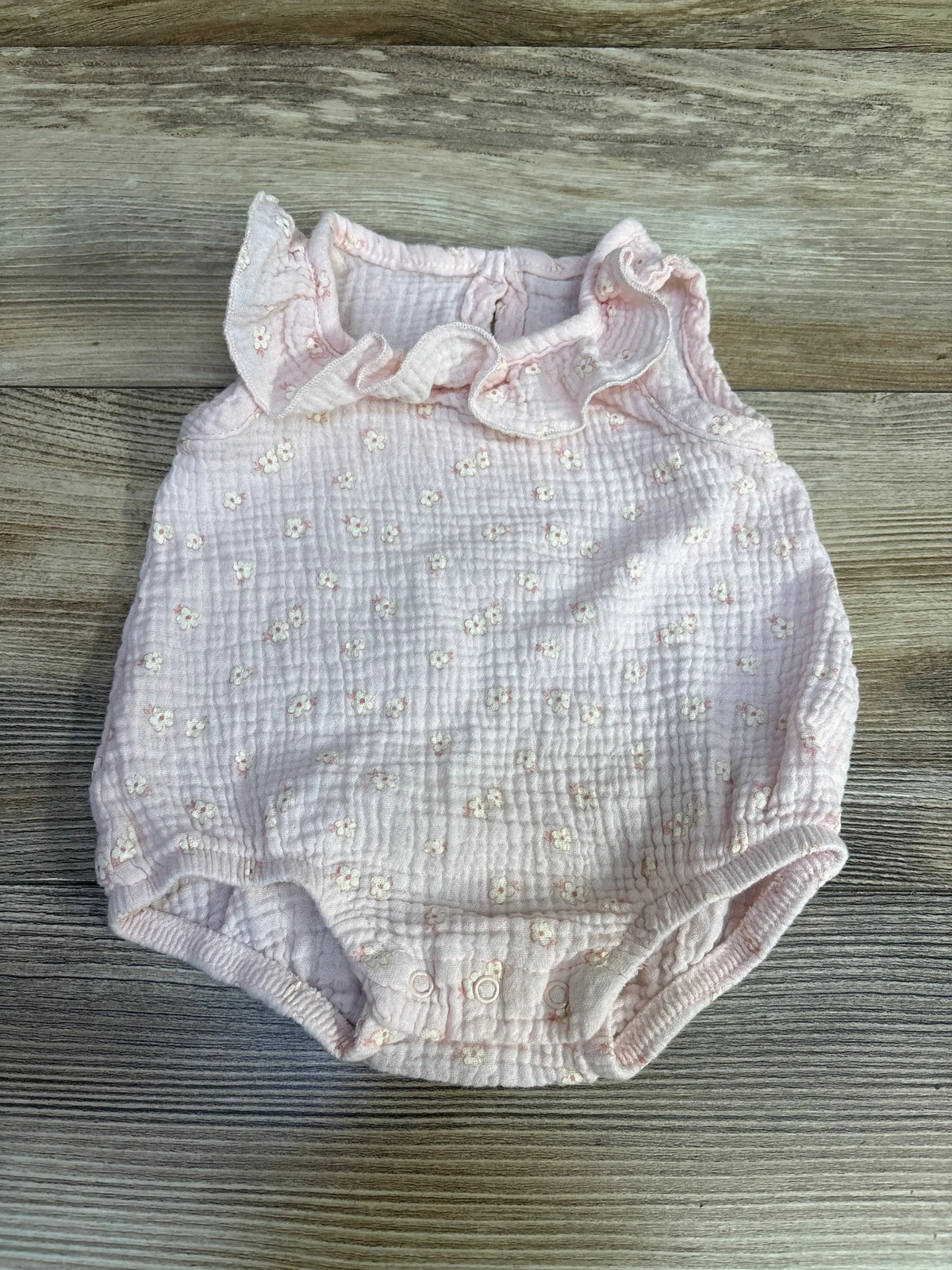 Front view of Chick Pea Floral Bubble Romper Pink sz 6-9m showcasing pale pink muslin with embroidered daisies and ruffled neckline on wood plank floor