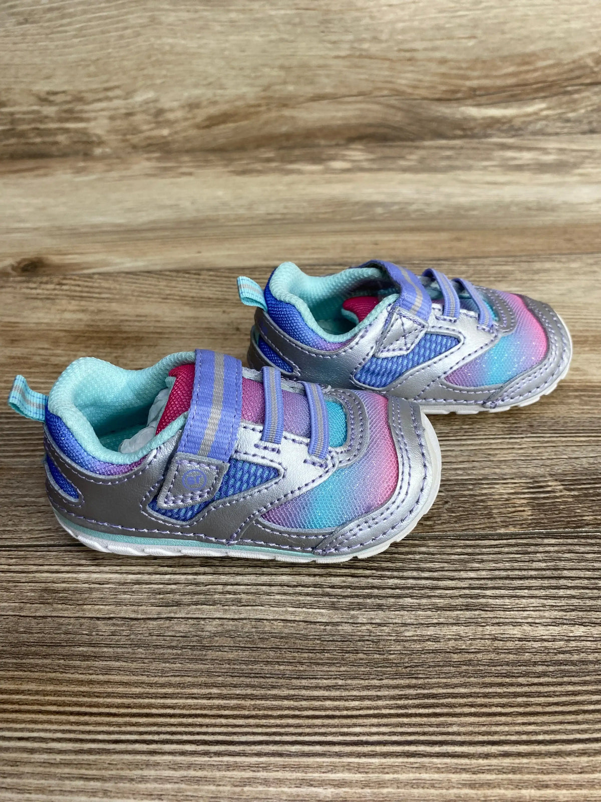 Side view of Stride Rite Adrian toddler sneakers size 4C showcasing metallic silver and pastel ombré upper with double hook-and-loop straps on wood background