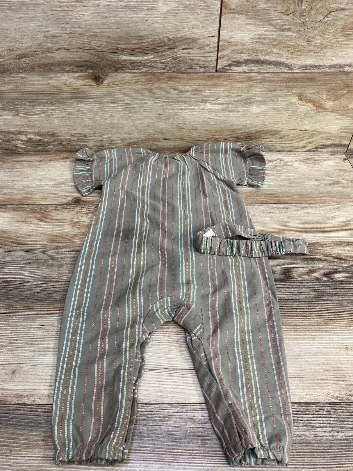 Flat lay of Penelope Mack olive coverall with metallic stripes, ruffle sleeves, elastic ankles and matching headband on wood