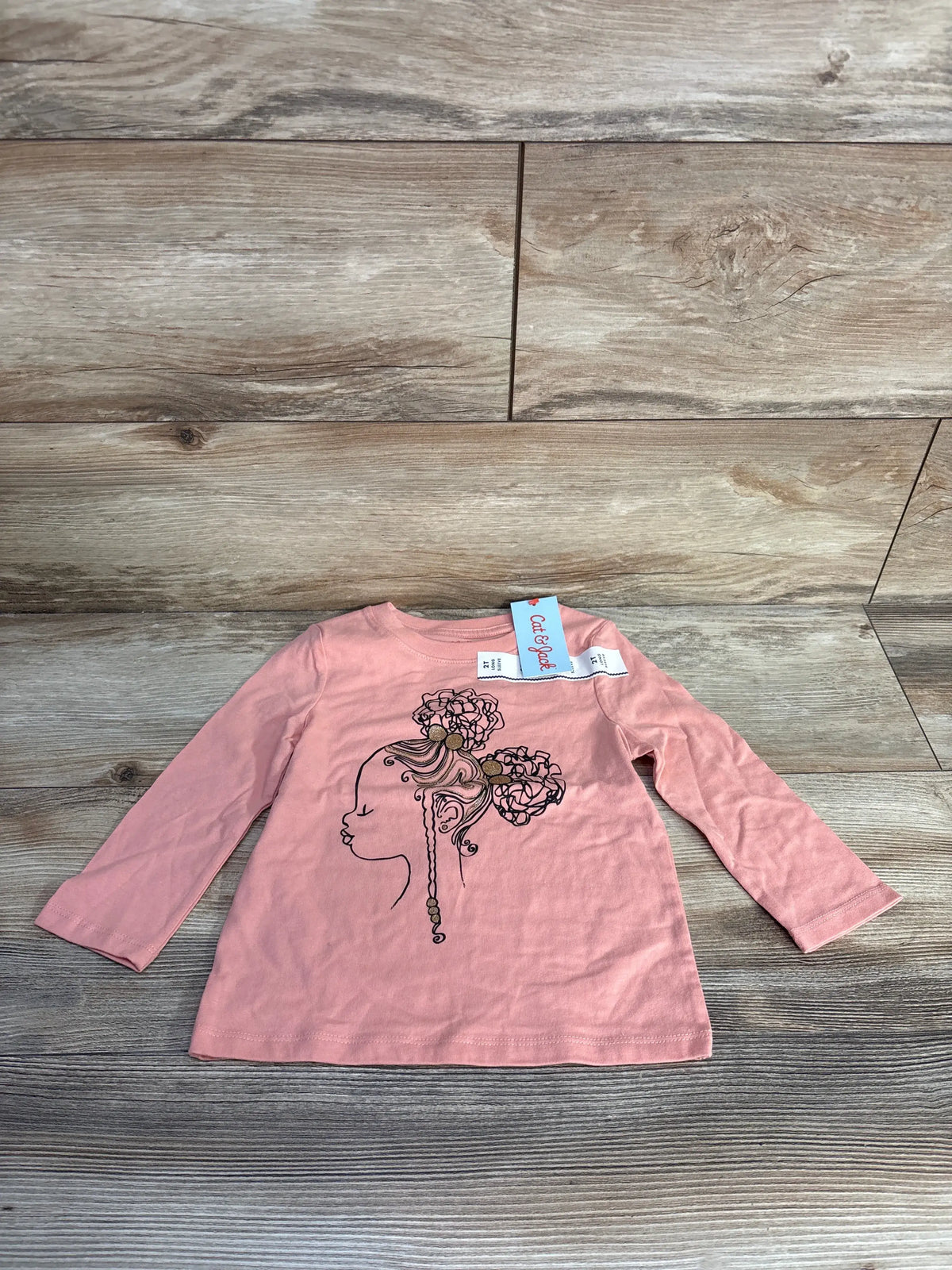 Front view of a pink Cat and Jack long sleeve shirt in size 2T showcasing a floral profile graphic on a wood floor