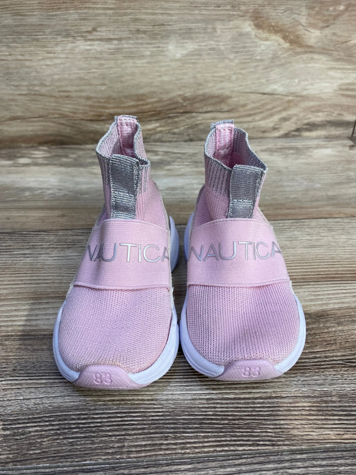 Front view of Nautica slip-on sock-style sneakers in pink with silver logo straps, knit uppers, and white soles on wood
