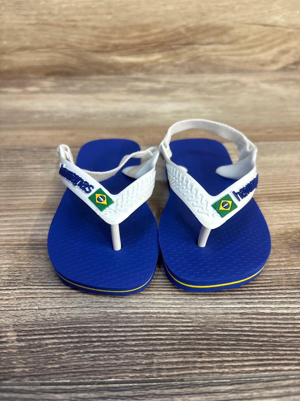 Blue and white toddler sandals with Brazilian flag accents on a wood background