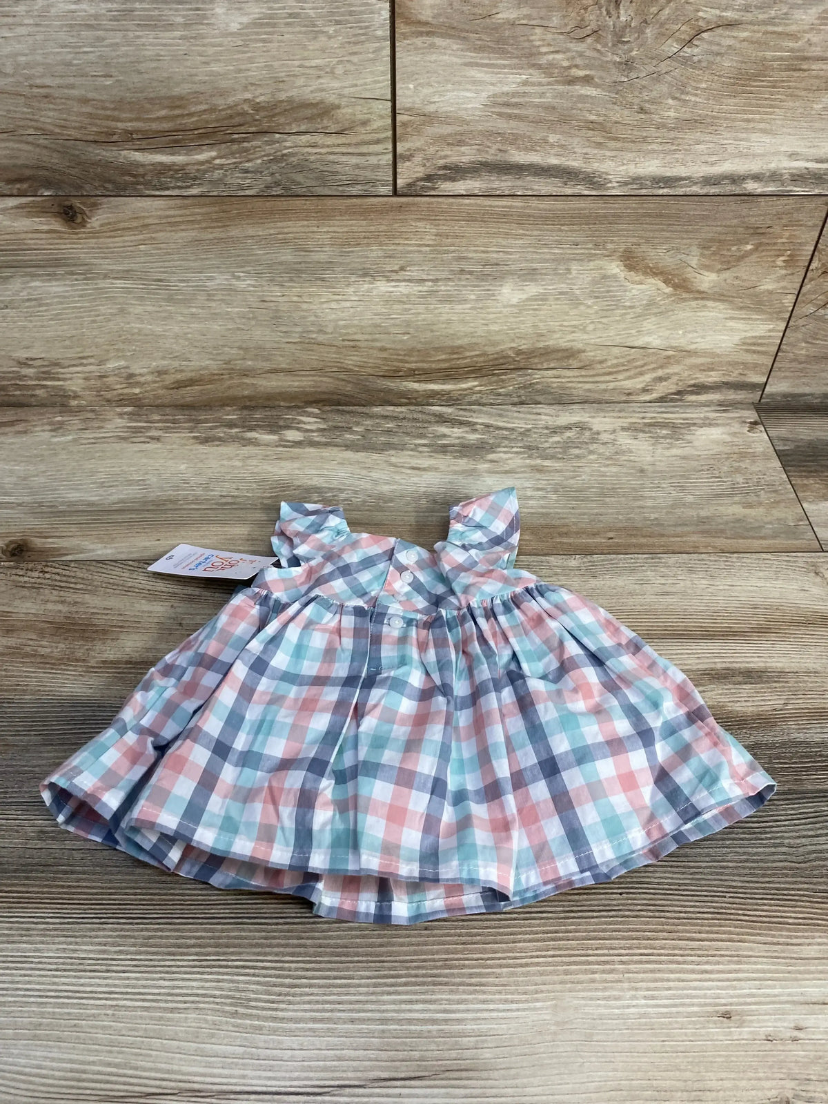 Flat lay of Just One You 2-piece plaid baby dress and matching bloomers, newborn size, pastel pink, teal, and gray plaid on wood background