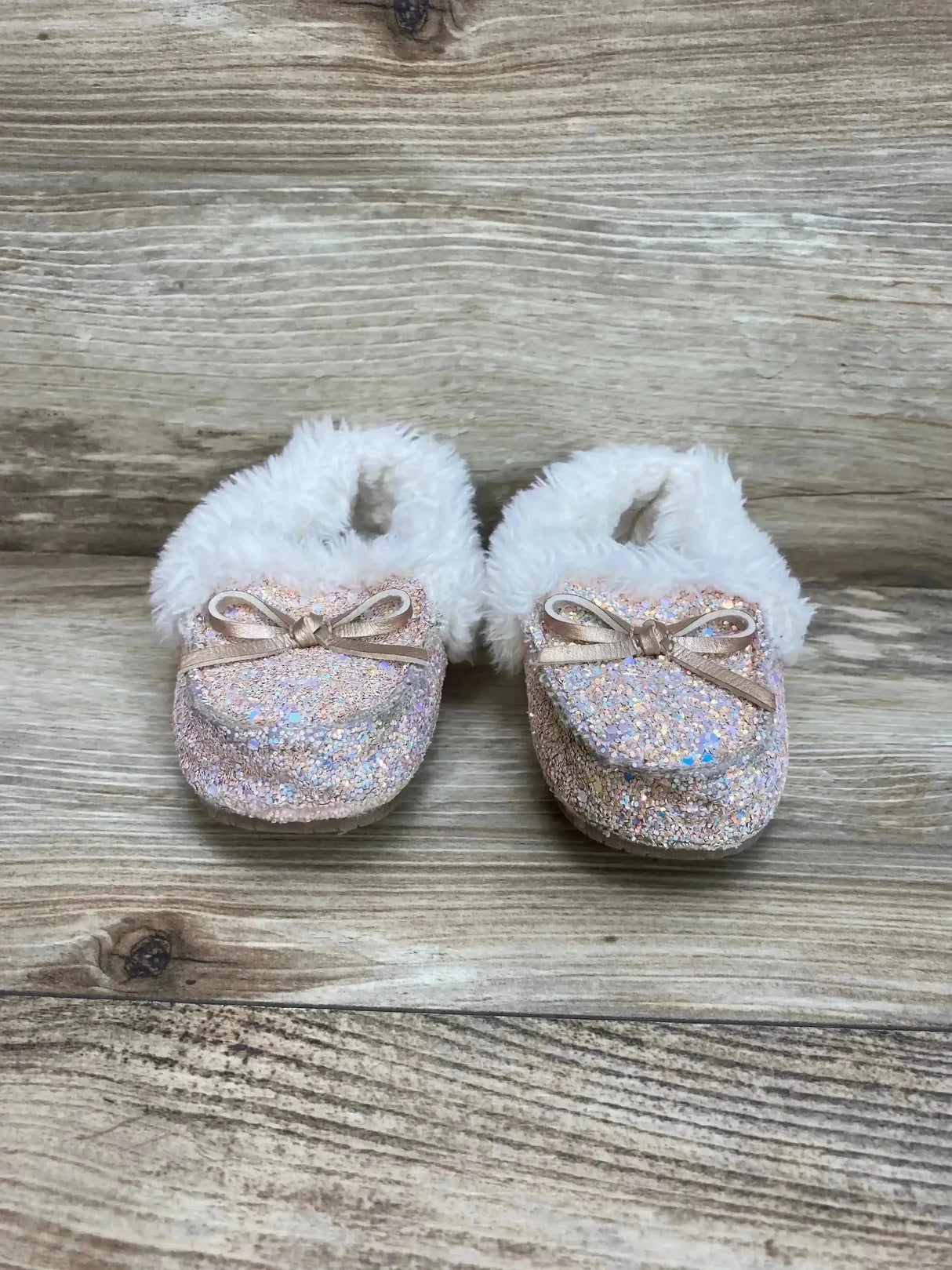 Front view of Cat & Jack Medora slippers size 6C, pink iridescent glitter with faux fur cuff and bow on wood background