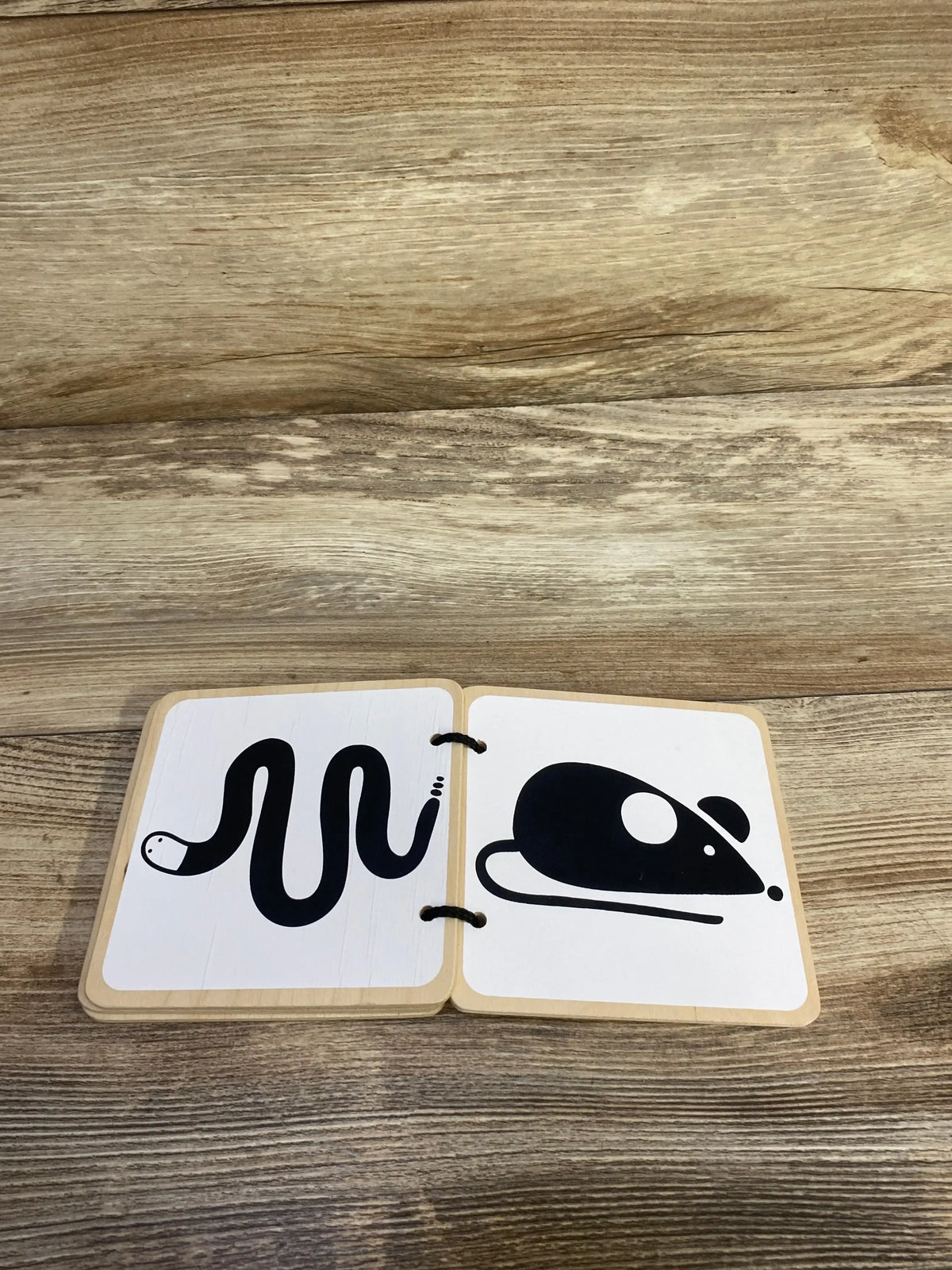 Open view of Lovevery Wooden Book showcasing black-and-white snake and whale illustrations on wooden pages with a wood-grain background
