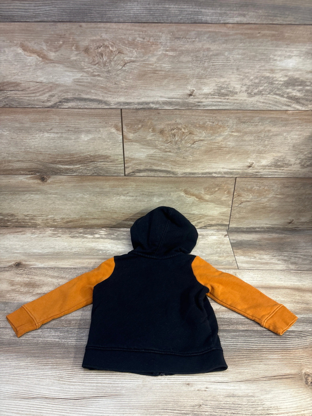 Back view of Cat & Jack full-zip jacket in black with orange sleeves and hood on a wood floor