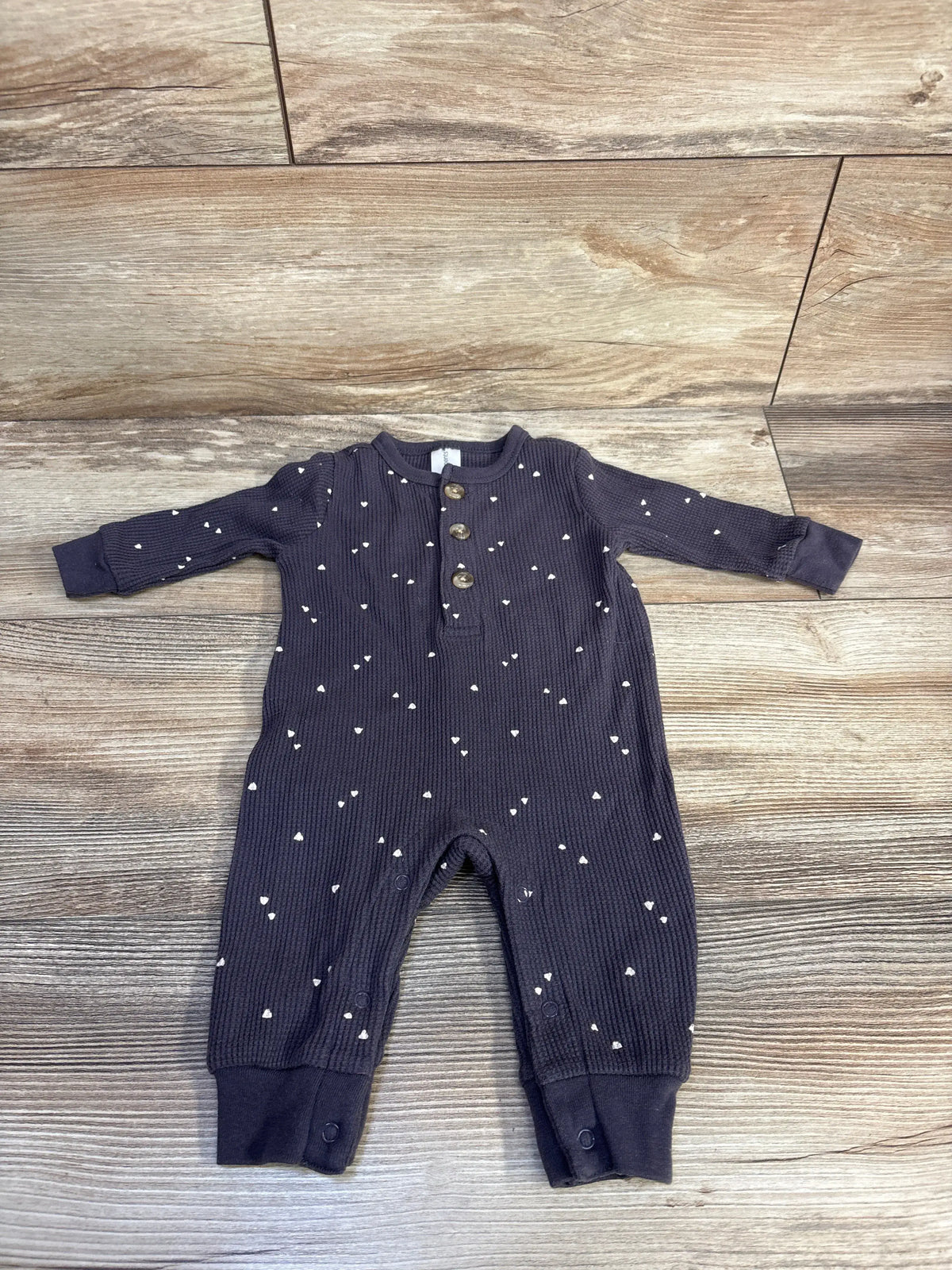Front view of Modern Moments grey waffle knit henley coverall with button placket and white heart pattern on wood-look floor