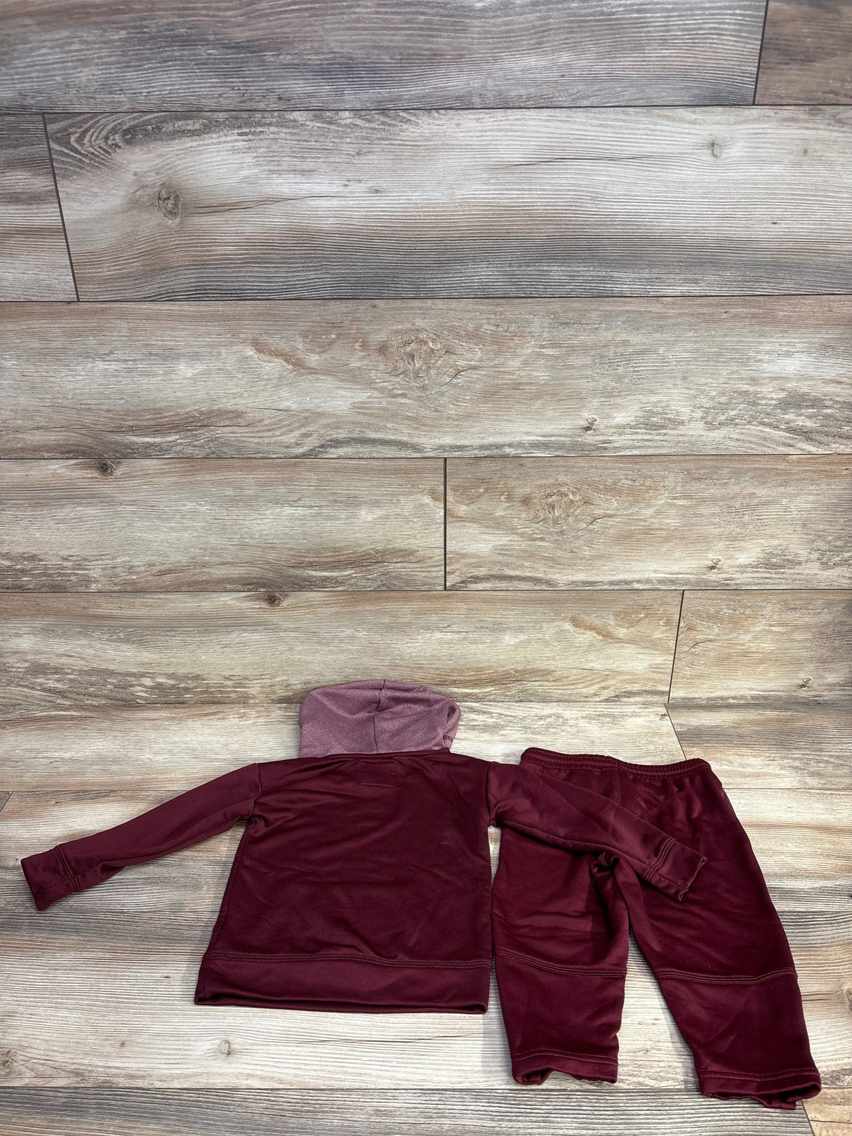 Maroon children's hooded jacket and matching pants set laid flat on wooden floor