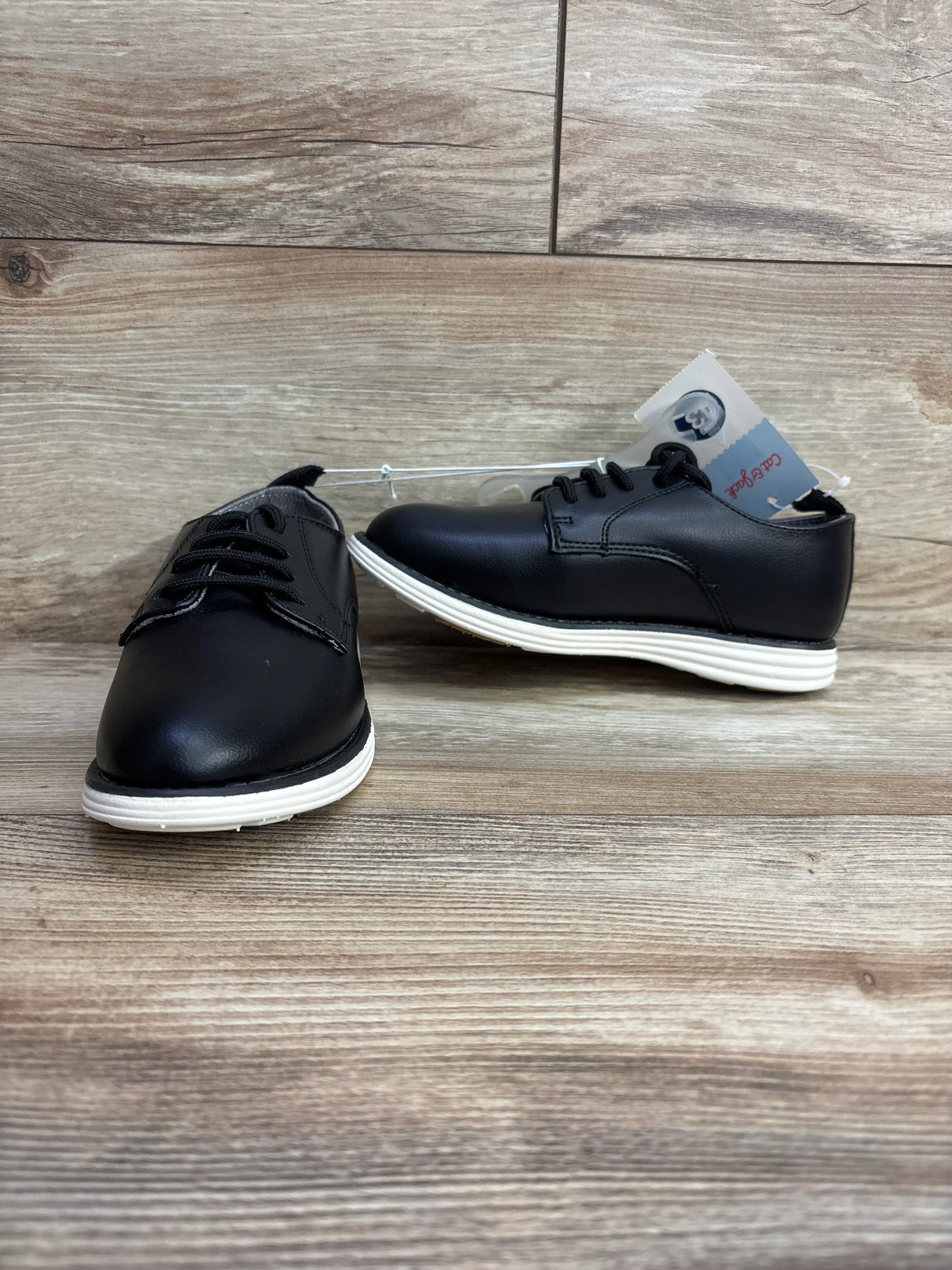 Three-quarter view of Cat & Jack Alfi toddler black dress shoes, size 13C, showing white rubber soles and lace-up design on wood surface