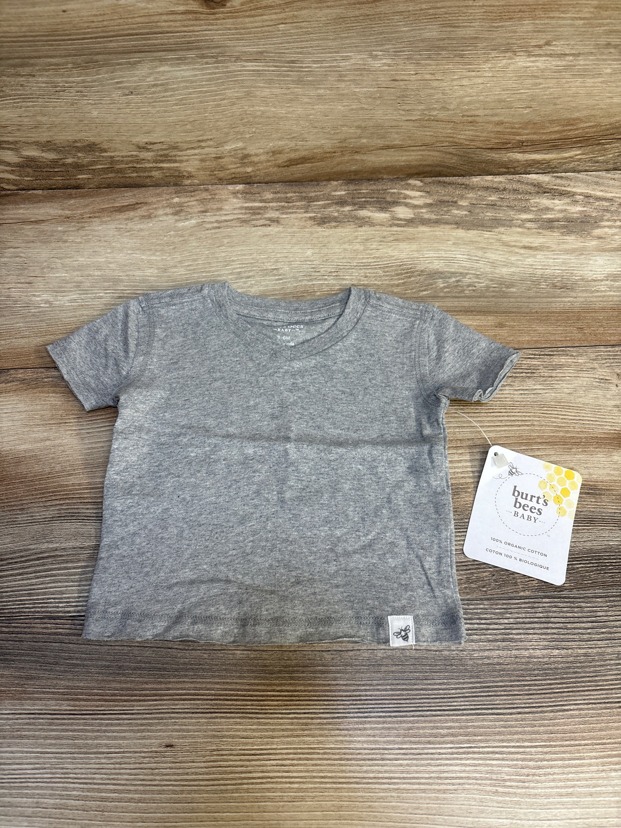 Flat lay of gray Burt's Bees Baby short-sleeve raw hem shirt showing brand tag on wood background