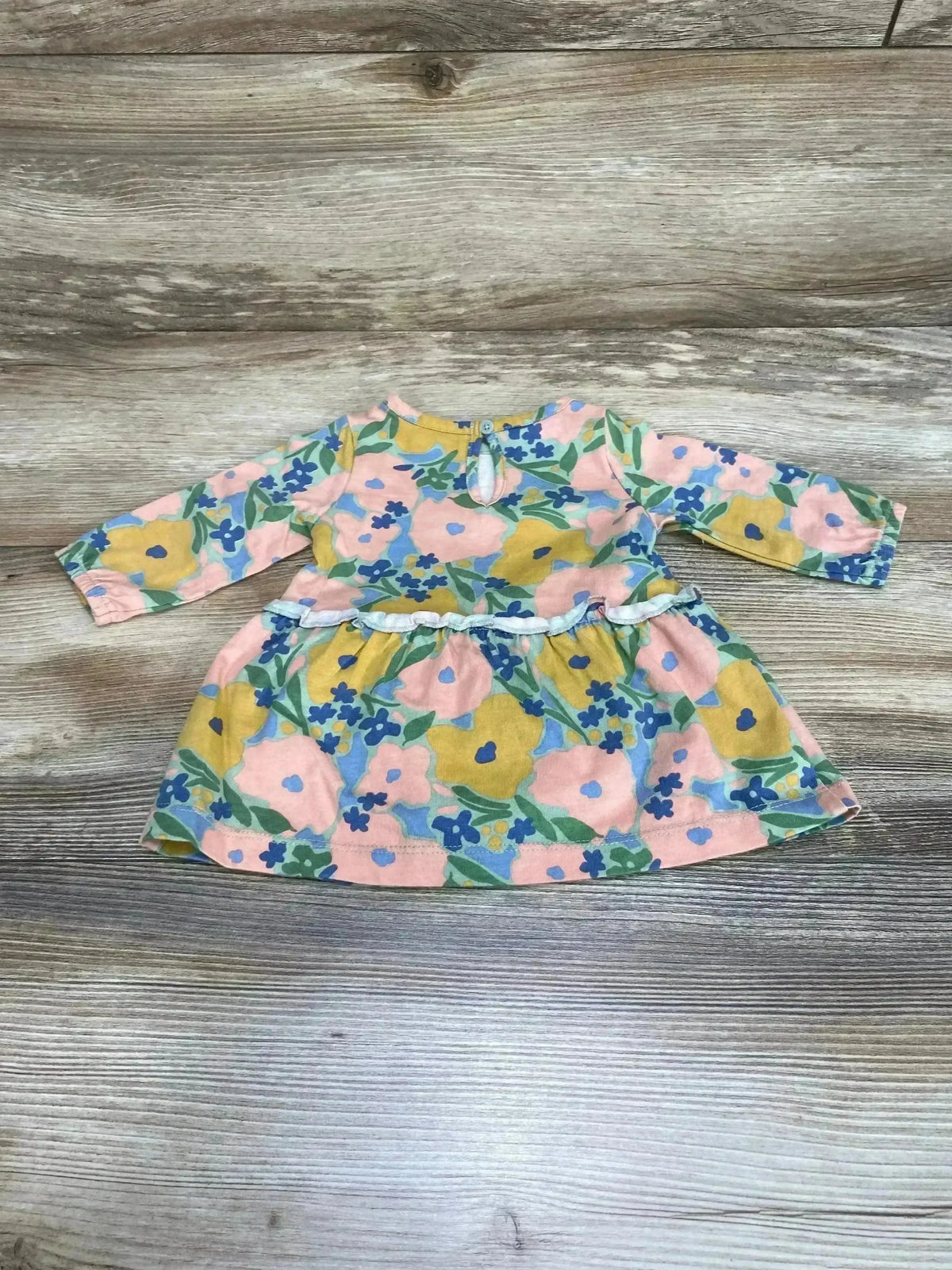 Flat lay of baby long-sleeve floral dress and matching bloomers showing pink, yellow, and blue flowers and ruffle waist on wood background