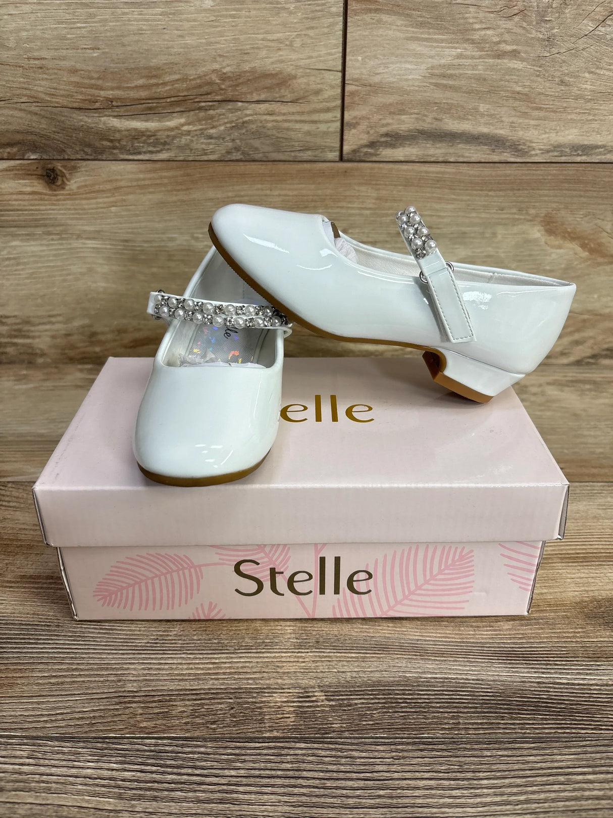 White patent leather girls' dress shoes with decorative pearl straps on a pink Stelle shoe box
