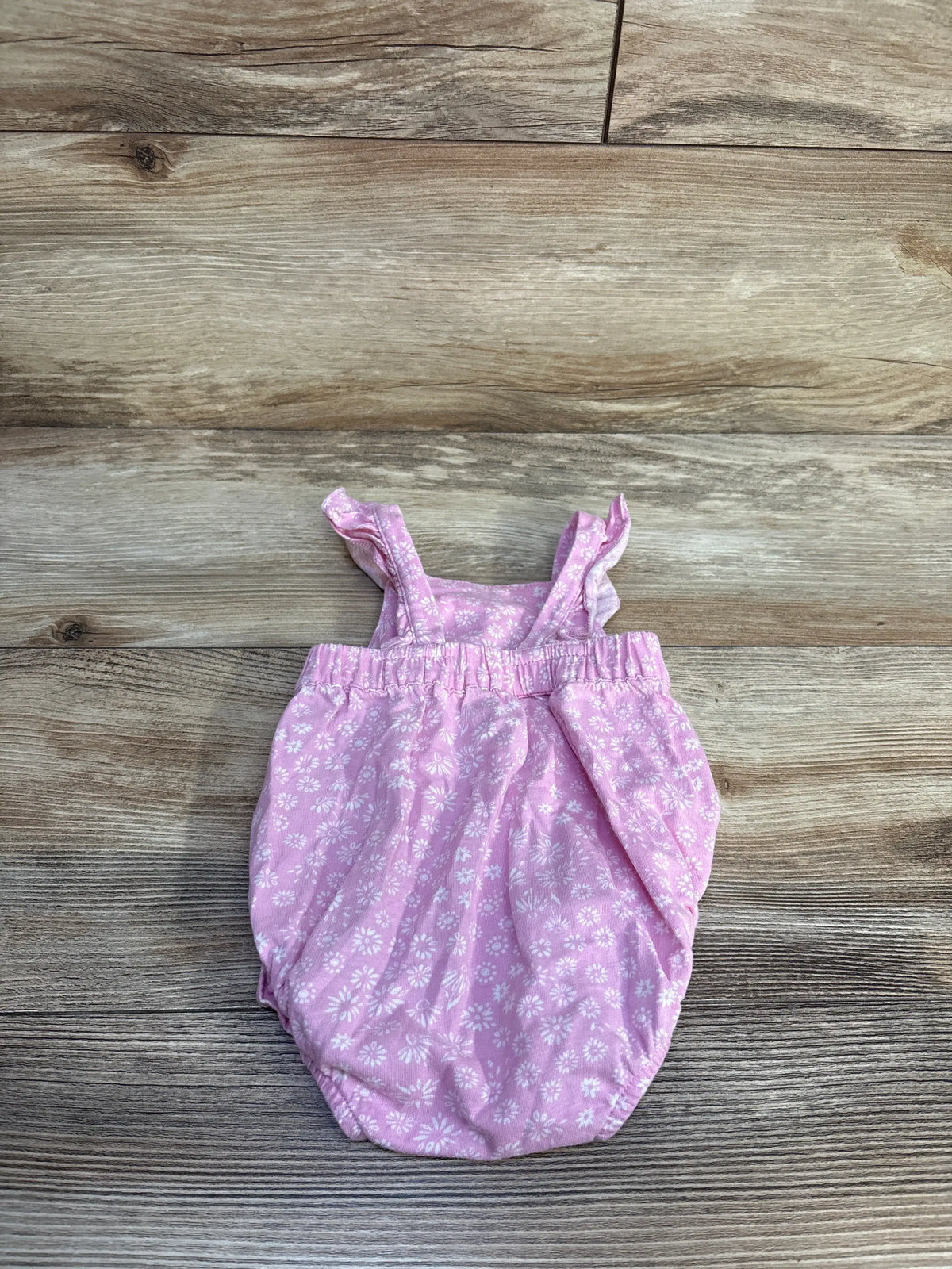 Front view of Carter’s pink floral bubble romper with white floral detailing and ruffled straps on a wood background