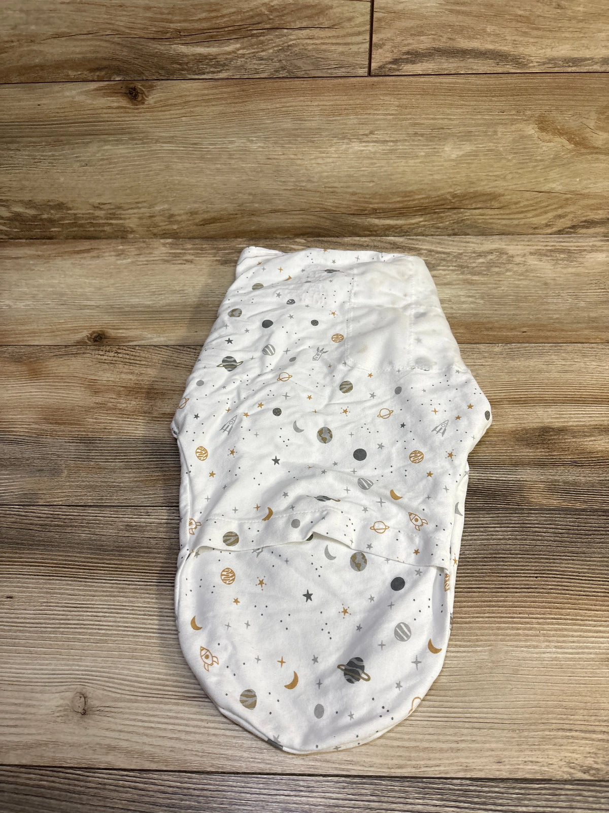 Top-down view of Swaddle Me Space Swaddle Wrap, white with gray and gold space print on wood background