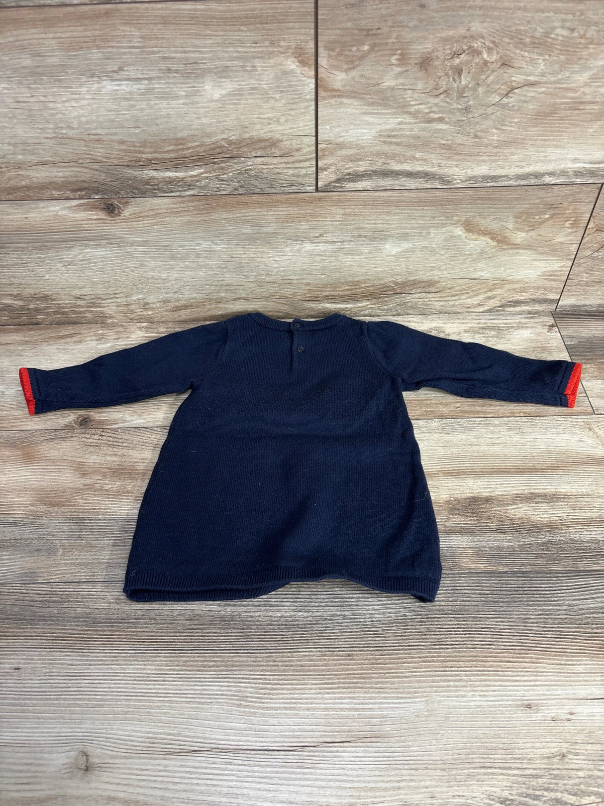 Navy blue long sleeve toddler dress with red cuffs on wood background