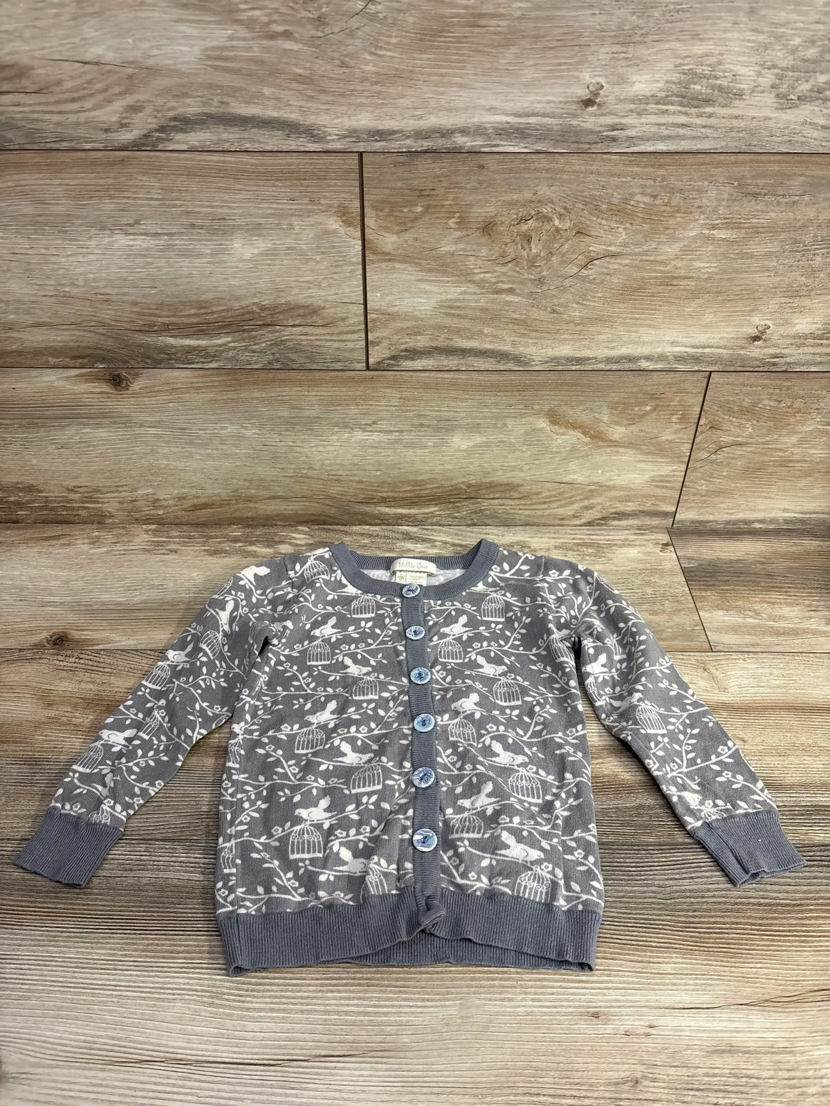 Gray button-up children's cardigan with bird and birdcage pattern on wooden background
