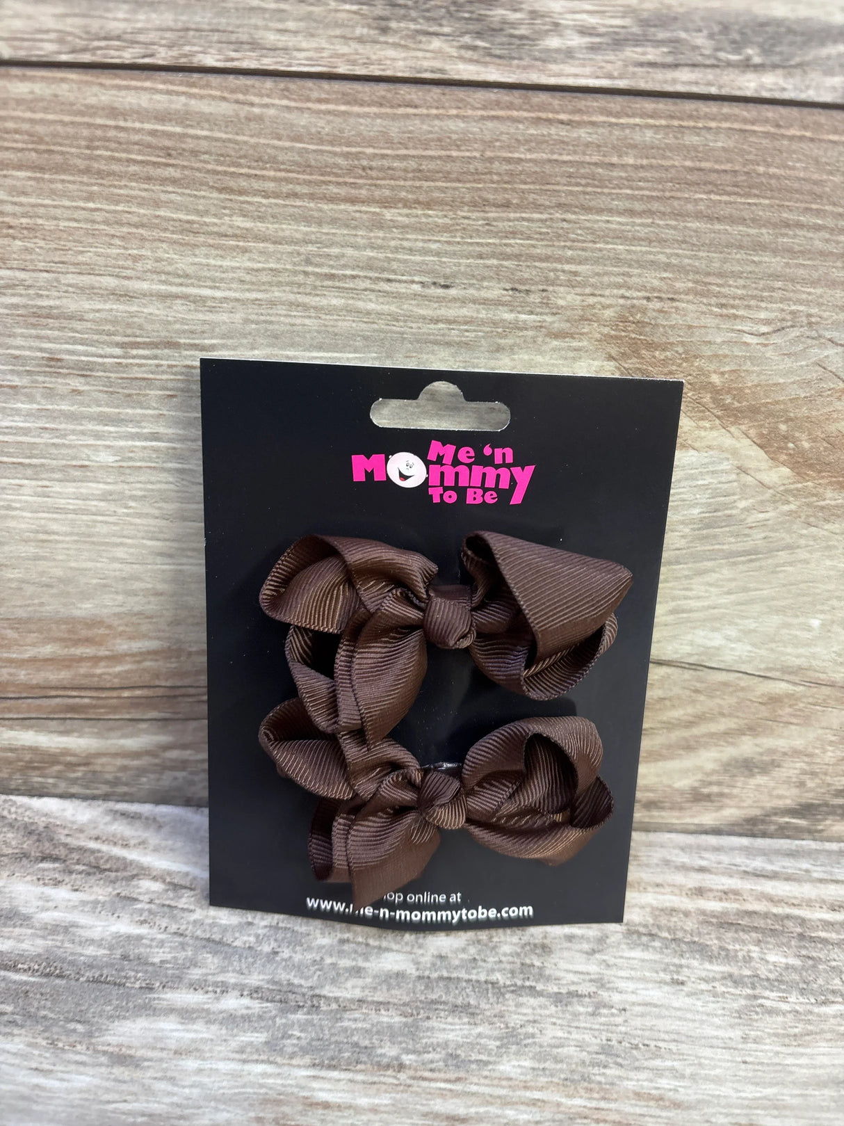 Front view of two brown grosgrain ribbon hair bows 2 pack on a black Me n Mommy To Be card against a wood background