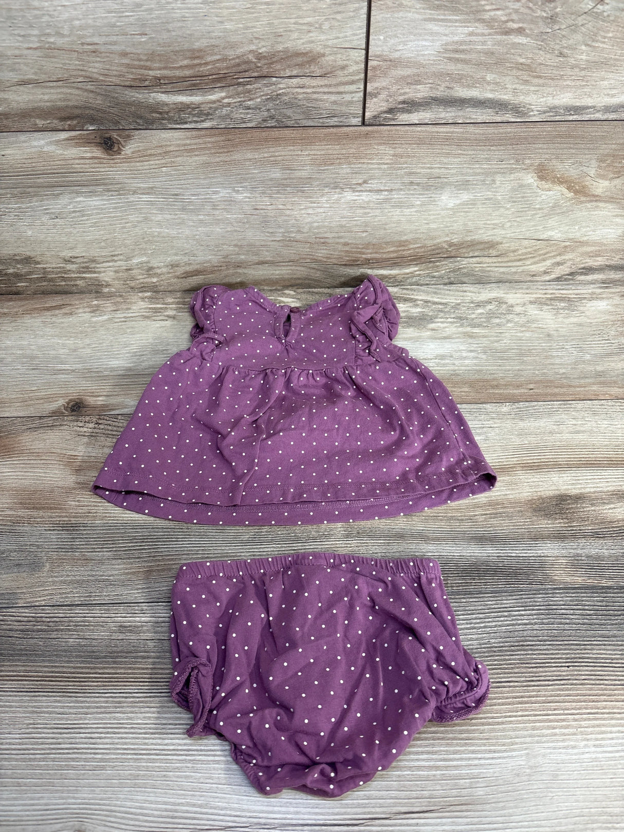 Flat lay of Carters 2pc Ruffled Polka Dot Dress and Bloomers Set in mauve with white dots and ruffle bodice on wood plank floor