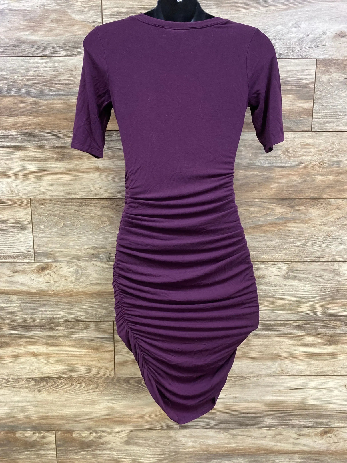Front view of purple Motherhood Maternity bodycon dress showcasing side ruching and asymmetrical hem on wood background