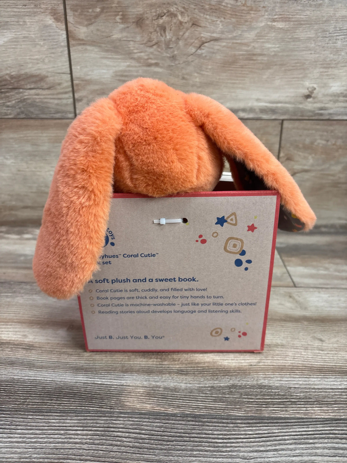 Back view of Happyhues Coral Cutie board book and plush bunny set with orange plush bunny and illustrated box on wood-look background