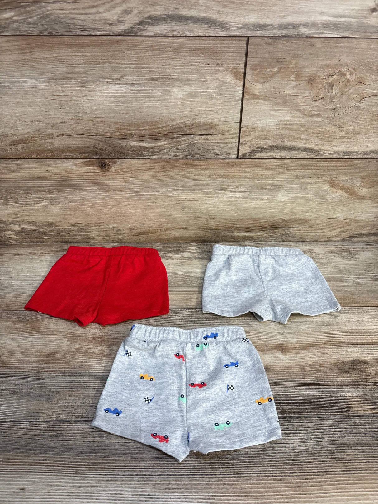 Set of three toddler shorts on wood floor, including red, grey, and car print designs.