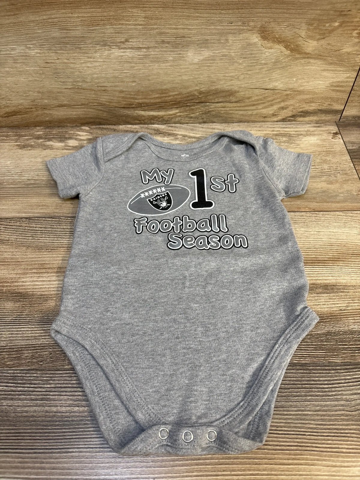 Gray baby bodysuit with "My 1st football season" and a football graphic on wood background
