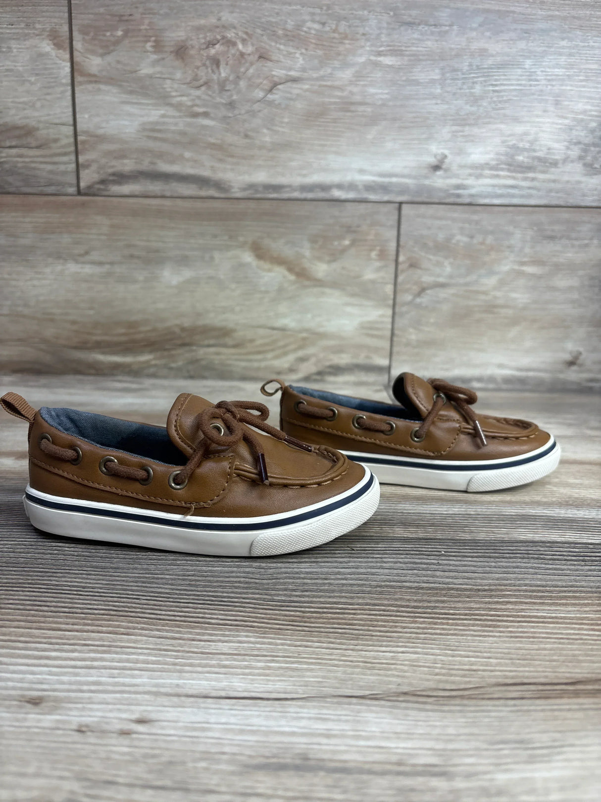 Pair of brown toddler boat shoes with white soles on wood flooring, children's resale store item