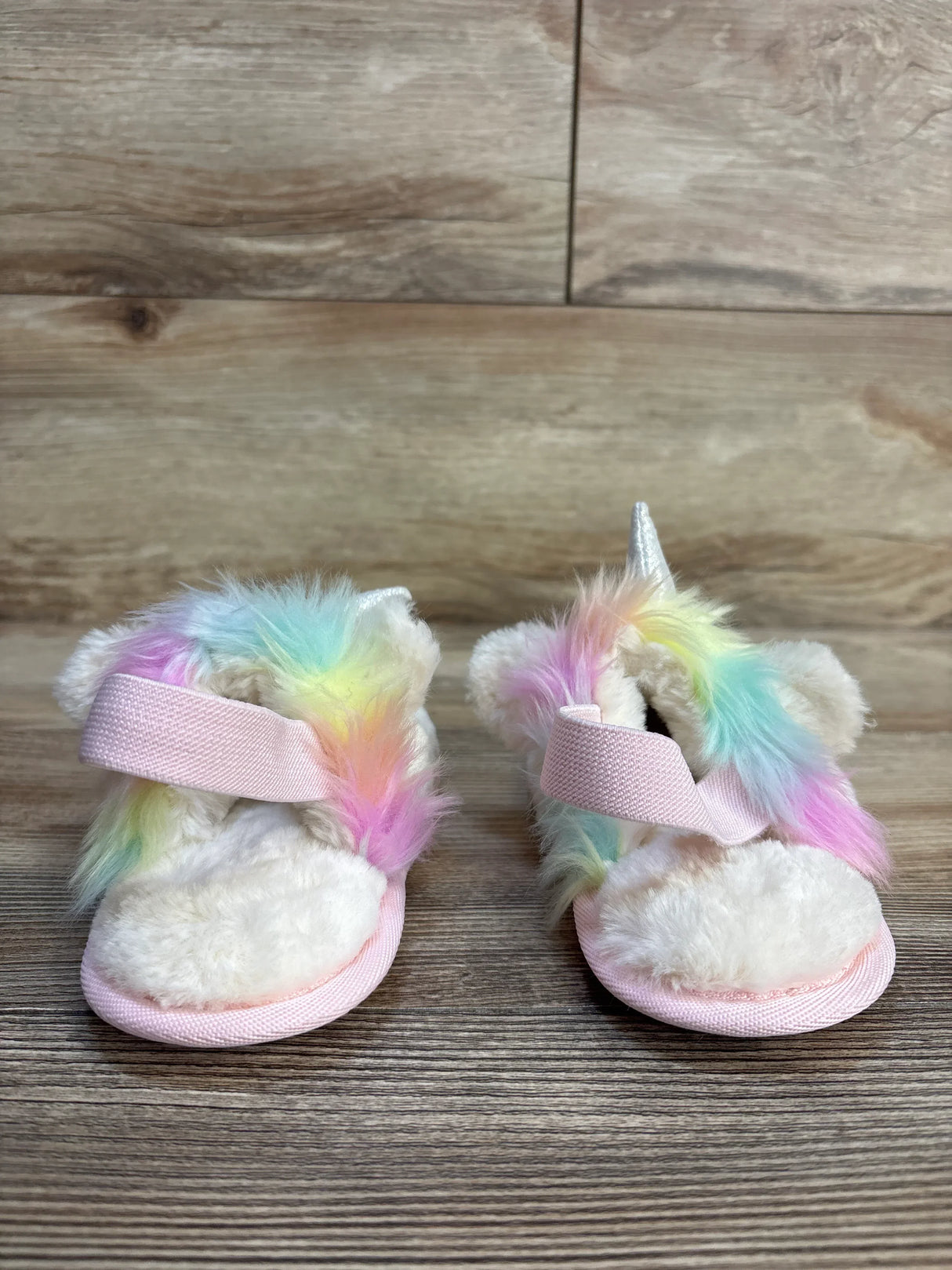 Adorable unicorn baby sandals with rainbow fur, pink straps, and silver horn on wood floor