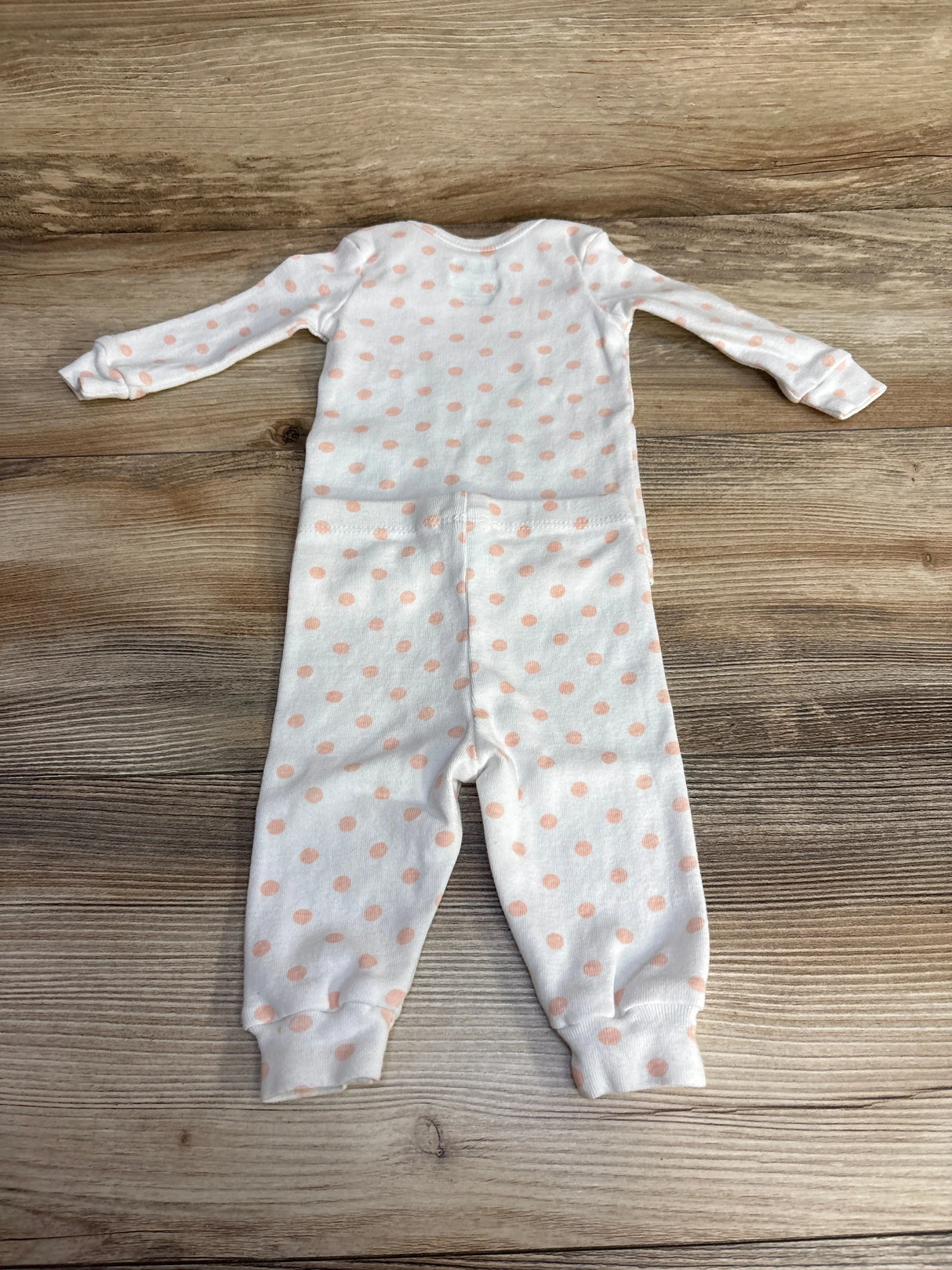 Flat-lay of white 2-piece polka dot infant pajama set showing long-sleeve top and cuffed pants with peach polka dots on wood background
