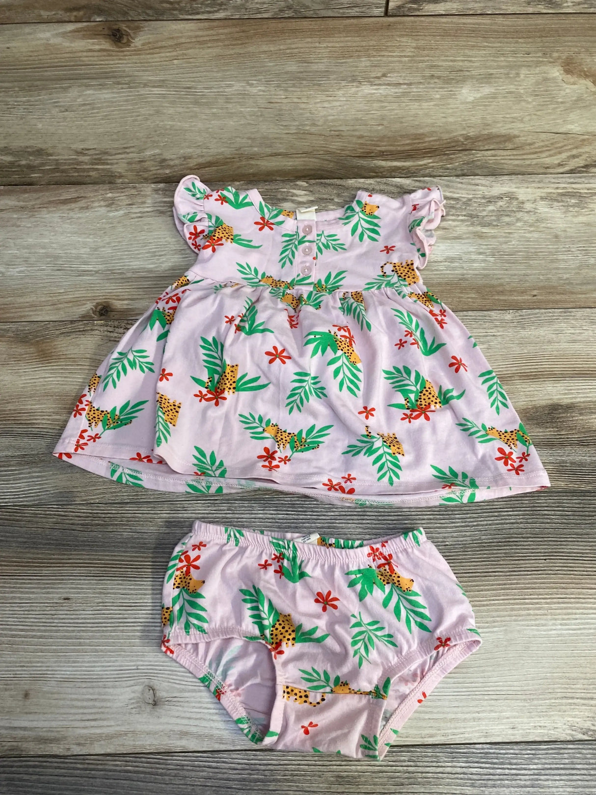Flat-lay pink henley dress with front buttons and flutter sleeves, plus matching bloomers with leafy cheetah print on wood